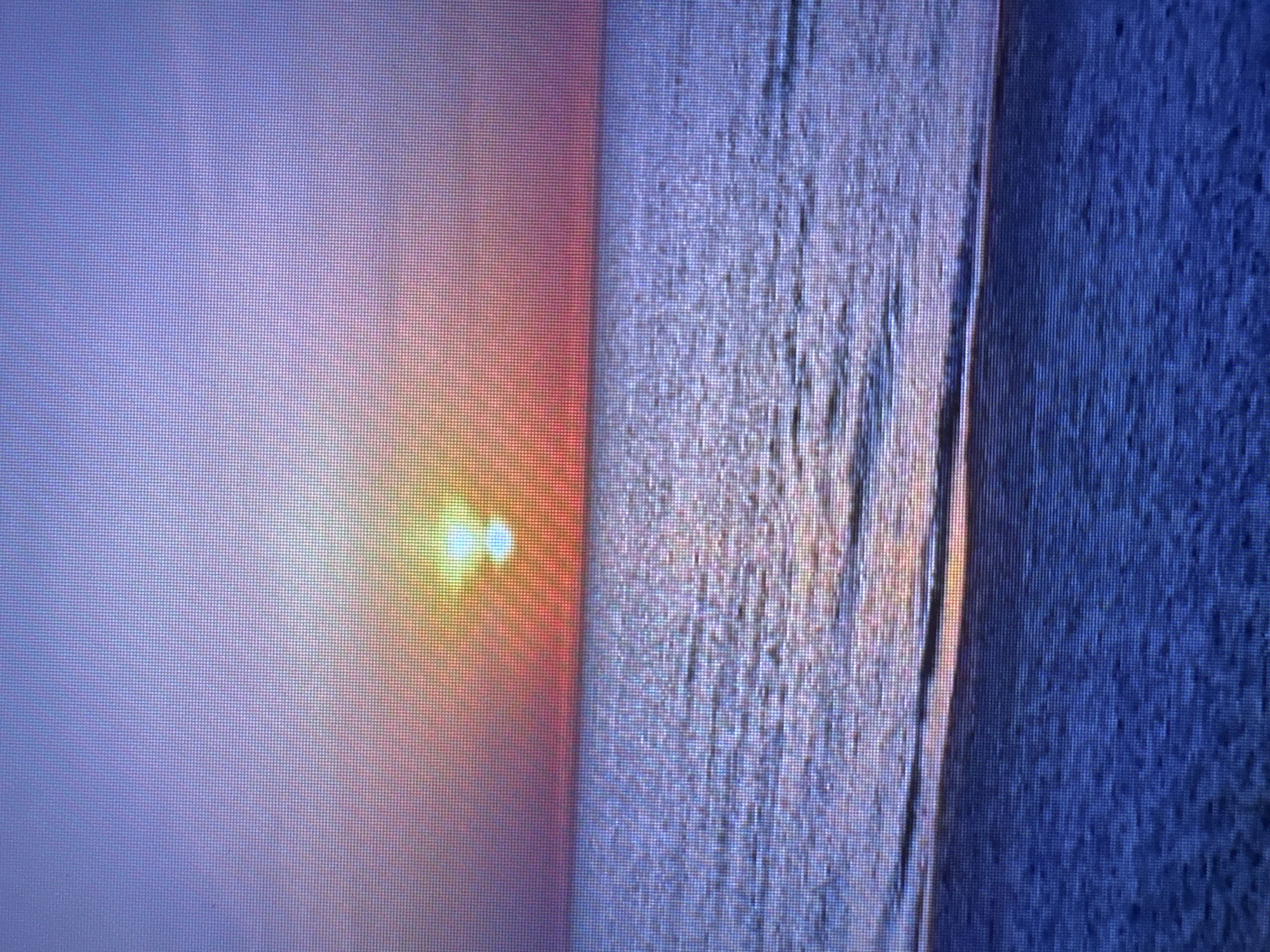 This is a photograph of a sunset over the ocean. The sky is a gradient of pink, orange, and purple, with the sun appearing as a bright yellow orb near the horizon. The ocean is a deep blue with gentle waves reflecting the colors of the sky. The foreground is a sandy beach, also in shades of blue and purple, with some texture visible. There are no people or objects visible in the image, and the environment appears to be a natural beach setting. The image is pixelated, suggesting it may be a digital photograph displayed on a screen. The question asks to include the location in the city of Perm, Russia. However, there is no indication in the image or the crops that this scene is located in Perm, Russia. It appears to be a generic beach sunset.