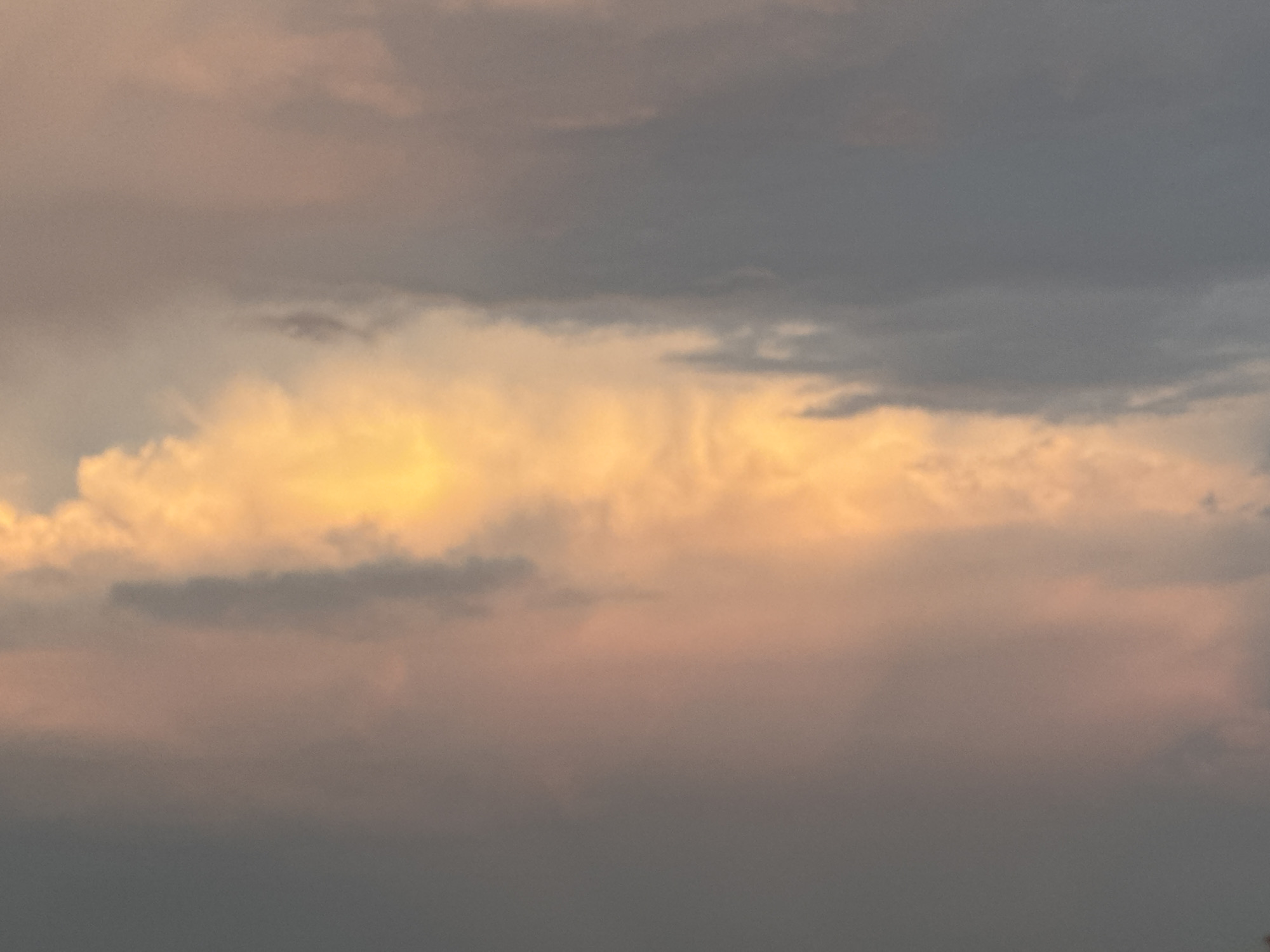 The image shows a cloudy sky at sunset. The clouds are illuminated by the setting sun, casting a warm, golden glow on some of the clouds, while others are a deep gray. The sky appears to be a vast, open expanse with no visible structures or landforms. The location is given as Syrt, Russia, suggesting a rural or natural setting where such cloud formations are common. There are no people or animals visible in the image. The scene is peaceful and serene, evoking a sense of natural beauty.