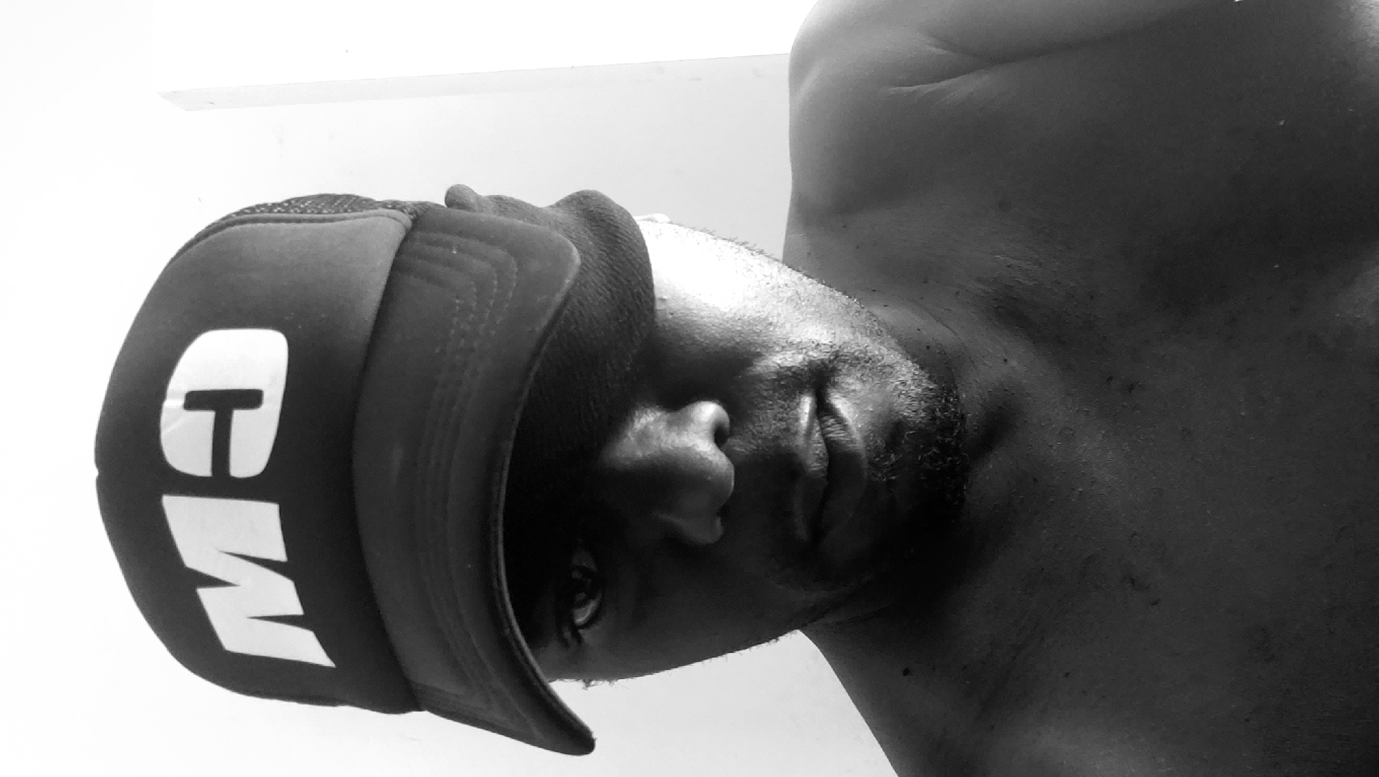 A black and white close-up photo shows a shirtless man wearing a cap with the letters "MW" on it. The man is looking at the camera. The location, Narayi, Nigeria, is not discernible from this image.