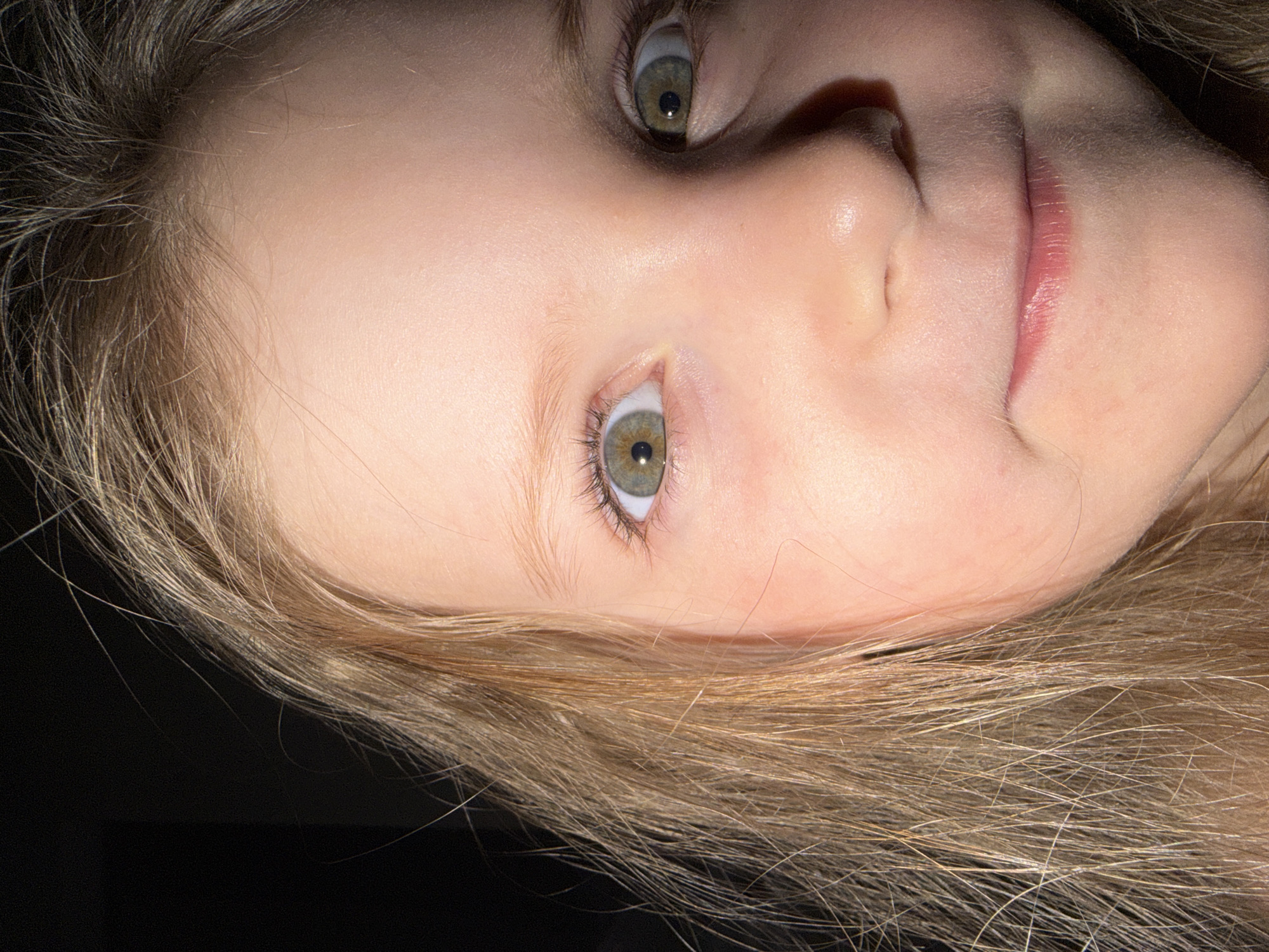 A close-up, rotated image shows the face of a fair-skinned child. The child has light brown or blonde hair and distinctive green eyes. Only the face and part of the hair are visible against a dark background. There is no indication of location within Chaikovsky, Russia.