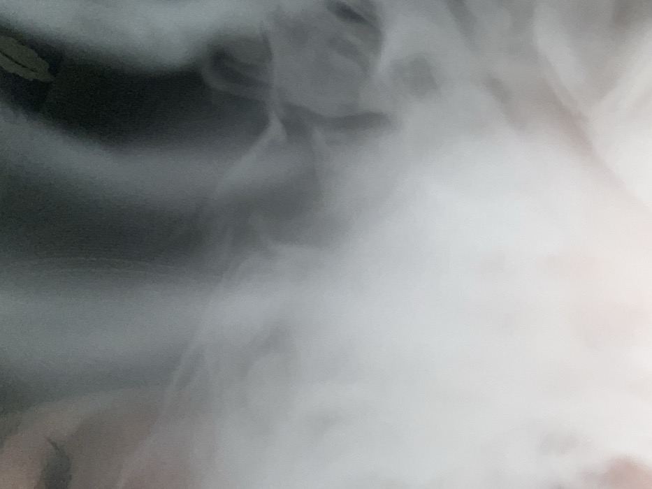 The image presents an abstract scene dominated by a large, diffuse white cloud or plume that occupies the lower and central portions of the frame, tapering into a darker, ambiguous background of grey and black in the upper and upper-right areas. The white element exhibits soft, undulating forms and blurry edges, suggestive of vapor, smoke, or a textured surface captured out of focus. Faint, irregular patterns and transitions are visible within the white and grey tones, creating a sense of depth and movement in the undefined substance. No identifiable people, distinct subjects, specific objects, or discernible actions or interactions are present within the frame. The environment is characterized solely by these contrasting tones and textures. This scene is located in the city of Chaikovsky, Russia.