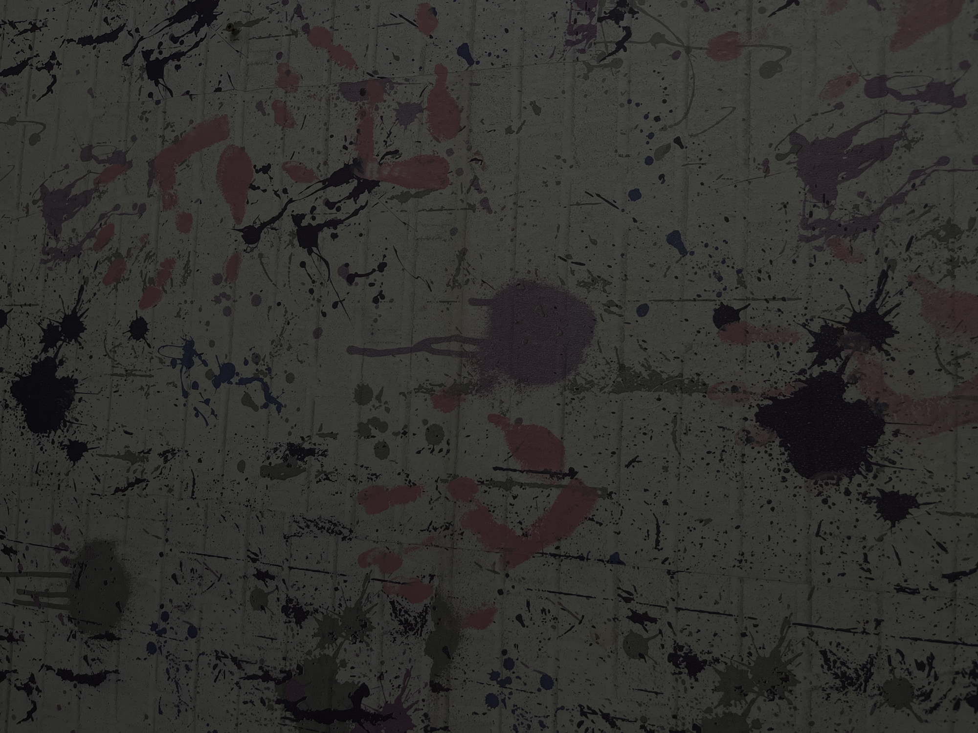 The image depicts a textured surface covered in a variety of colorful splatters and markings. The base surface appears to be a pale, possibly concrete or stucco wall, with vertical striations or lines running throughout. Splashes and drips of paint in shades of pink, purple, black, blue, and possibly green are scattered across the surface, creating an abstract and chaotic pattern. The image has a somewhat dark and muted tone. There is no information about the city of Maladzyechna, Belarus within the image. There are no people or discernible objects within the image. The action is suggested by the presence of the splatters, implying the act of throwing or splashing paint onto the wall. There are no visible interactions. The environment is confined to the immediate surface of the wall.