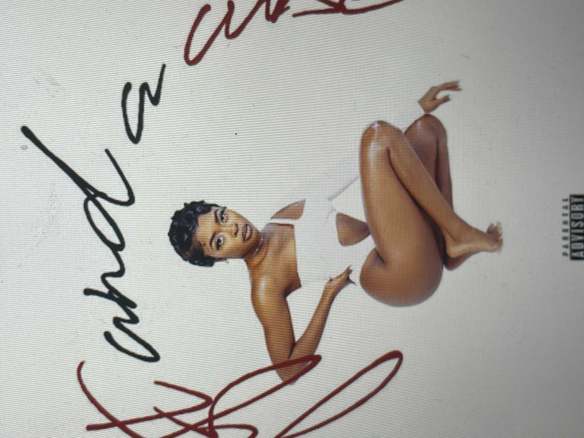 The image displays what appears to be an album cover, featuring a dark-skinned woman against a plain white background. The woman is positioned centrally, lying on her side or back, with her legs bent and crossed. She is wearing a simple white one-piece swimsuit or leotard. Her short, dark hair is styled, and she gazes directly at the viewer with a calm expression. Her skin appears smooth and slightly reflective, possibly oiled.
Stylized handwritten text in black is visible in the upper left portion of the image, appearing to spell out "and a". Below and to the left of the woman, more handwritten text in red cursive script is present; while partially obscured and highly stylized, it resembles words such as "kinda cool" or "kinda real." In the lower right corner, the black and white "PARENTAL ADVISORY EXPLICIT CONTENT" label is clearly visible. The overall aesthetic is minimalist, focusing primarily on the artist and the text.