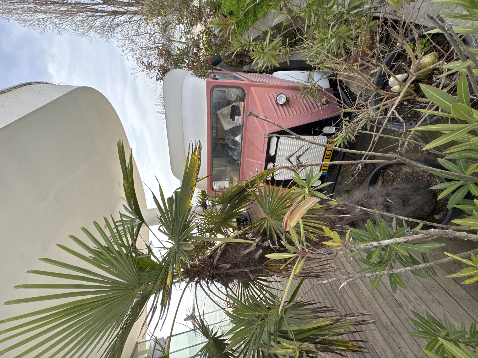 An exterior shot shows a reddish-pink Citroen van parked on a wooden deck. The van has a white roof and black and white grill. Green foliage obscures much of the van, which is parked near a white curved wall. A license plate is visible on the front of the van, reading "97 OGJ 55". The location is likely Varna, Bulgaria. The sky is overcast.
