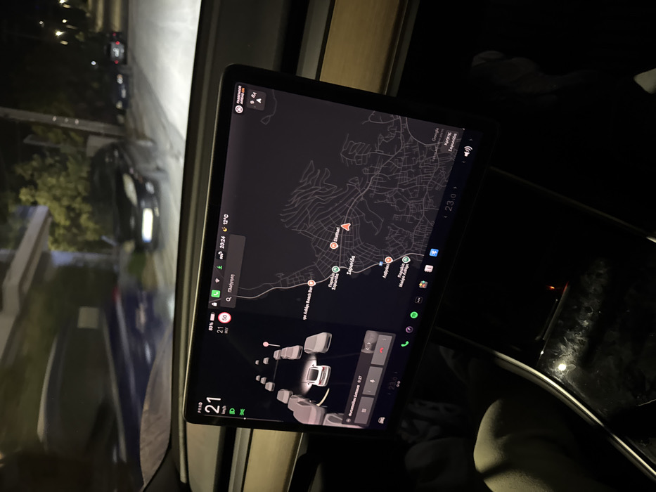 A screen displays navigation information within a vehicle. The map shows a route to Σαρωνίδα. The outside temperature is 12°C. The time is 20:24. The car's speed is 21 km/h. The battery level is 80%. The image indicates the presence of other vehicles in the vicinity, and the infotainment system shows a black interface. The current song is displayed as "Ρομαντισμός." The interior is dimly lit.