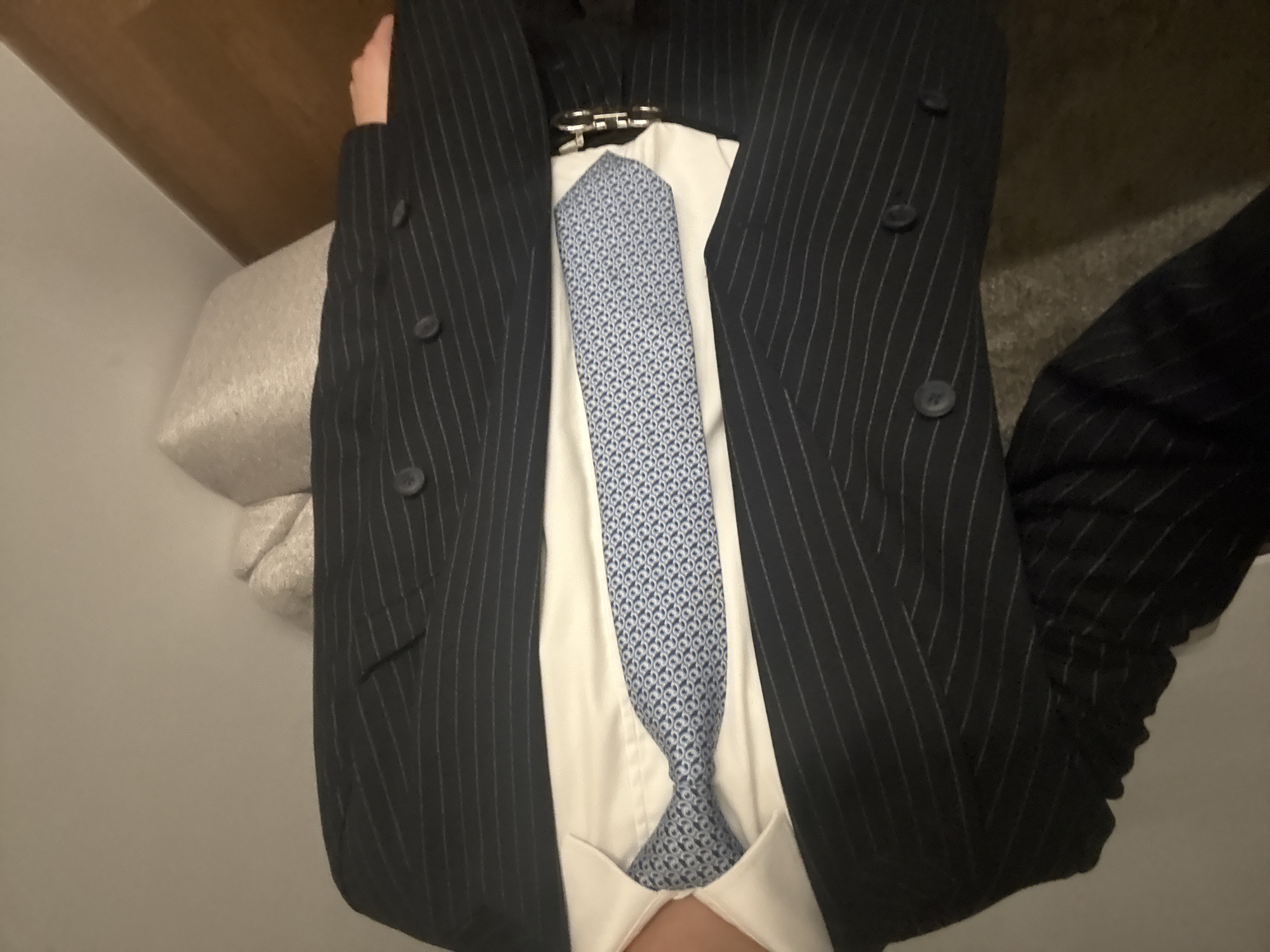A person is wearing a dark, pinstriped suit jacket over a white shirt with a patterned blue tie. The jacket is double-breasted with three visible buttons. The person's clothing is displayed in an indoor setting. There is no indication of the location being San Bernardino Tlaxcalancingo, Mexico in the image.