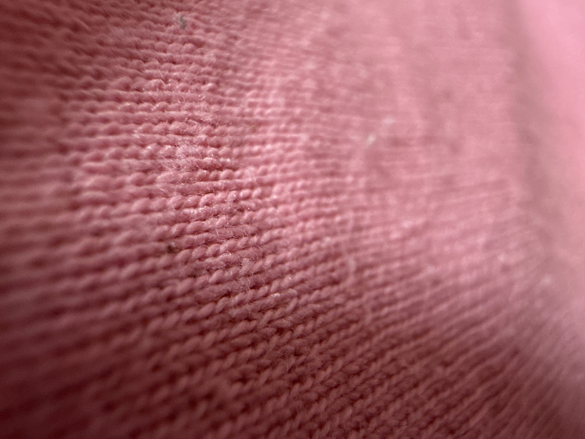 The image shows a close-up of a pink knitted fabric. The texture of the knit is visible, with individual loops and strands of yarn. The color is a muted, dusty rose. The depth of field is shallow, blurring the right side of the image. There are no people, subjects, objects, actions, interactions, or environmental details beyond the fabric itself. It is impossible to infer its location as Iarebichna, Bulgaria from the image alone.