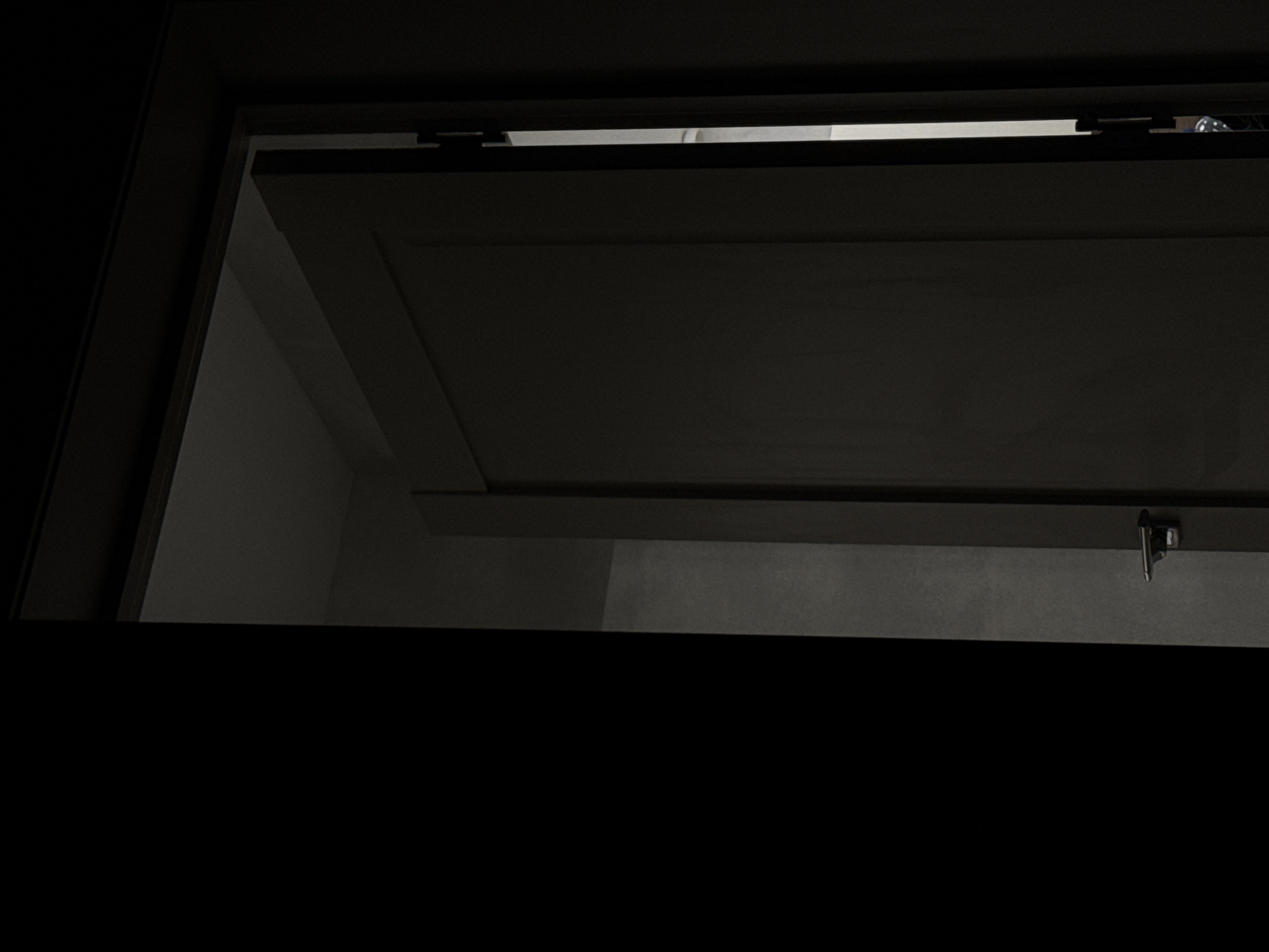 The image shows a partially open dark gray door. A sliver of light enters through the gap, revealing a dimly lit room beyond. The door has a brushed metal handle. The setting is a domestic interior, possibly a hallway or entryway. No specific location in Kaluga, Russia can be determined from the image.