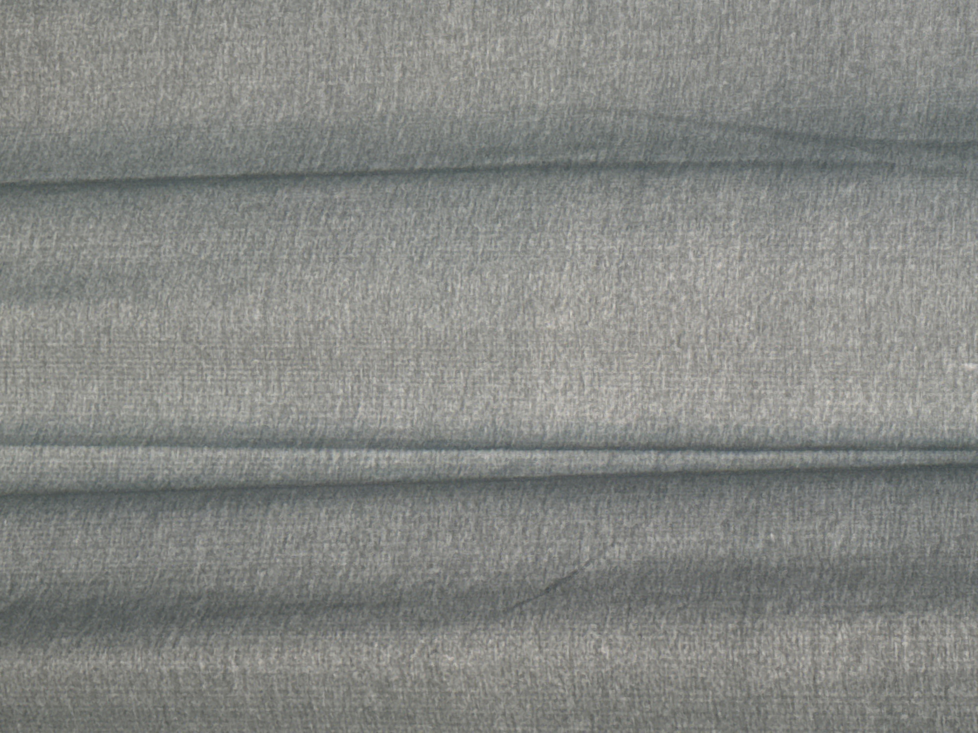 The image shows a close-up, abstract view of a textured, gray fabric. The fabric is draped, creating vertical folds and shadows. The texture appears to be a woven material with a slightly rough, matte finish. The lighting is soft, casting subtle shadows within the folds, which give the fabric a sense of depth. There are no people, animals, or discernible objects other than the fabric itself. The background is entirely composed of this fabric. The scene is devoid of any context that would indicate a specific location in a city.