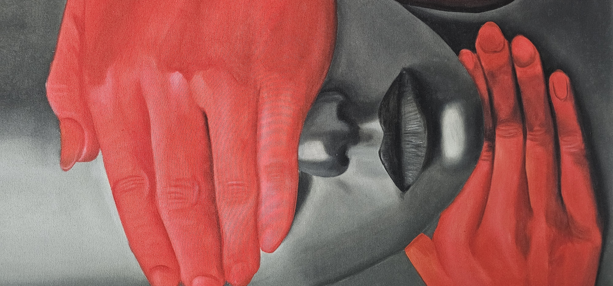 The image is an oil painting depicting a grayscale face being held by two bright red hands. The face is positioned horizontally, with the nose and lips visible in the center. One red hand is placed on the left side of the face, while the other is on the right. The painting appears to be on canvas, given the visible texture. There is no discernible information in the image to indicate a location in Denpasar, Indonesia.
