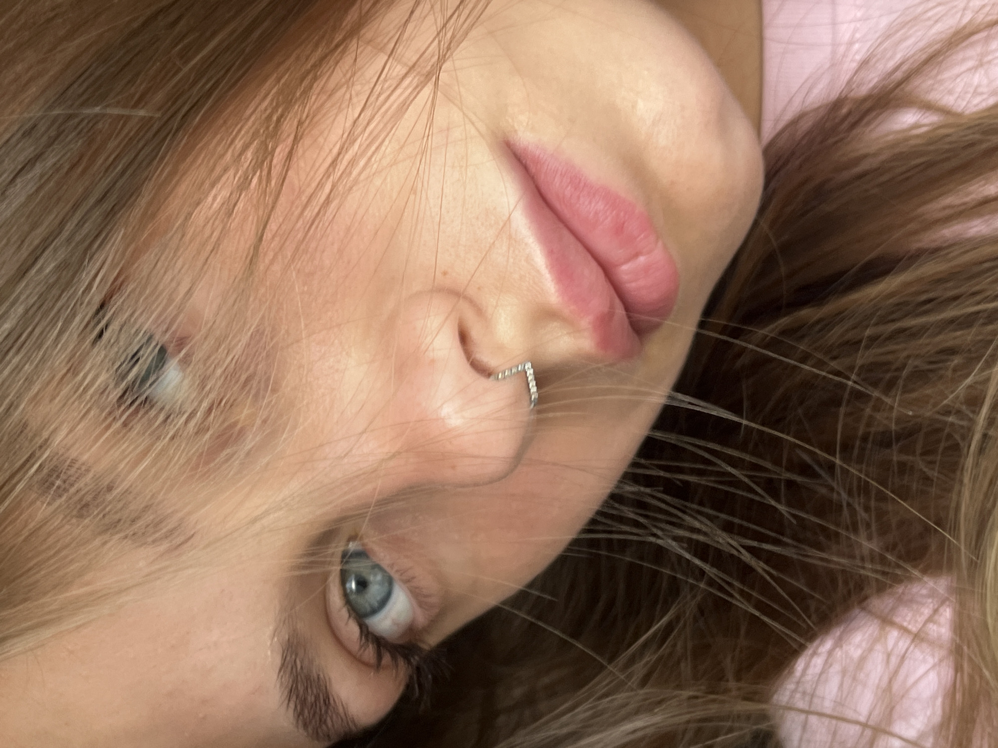 A close-up portrait shows a person with light brown hair and blue eyes. They have a small, silver nose ring. The background appears to be a pink surface. There is no evidence to place the image in Фоки, Russia, or any other specific city.