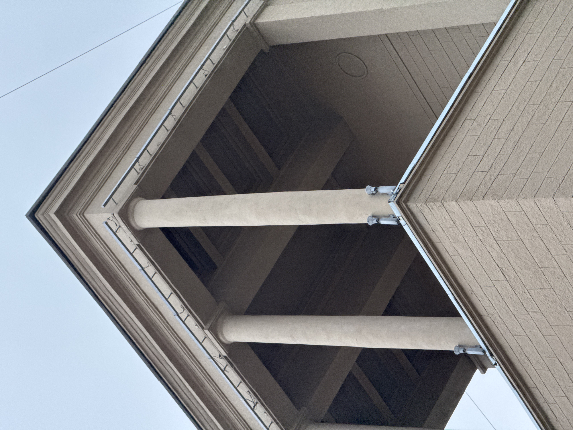 The image is a low-angle shot of architectural details, specifically the corner of a building with columns, a cantilever, and decorative molding. The building has a beige color scheme. The shot reveals an underside of the building, highlighting the construction and structure. The location is Moscow, Russia.