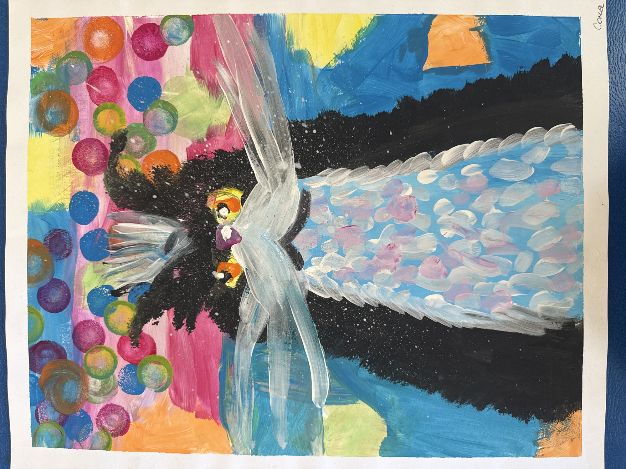 The image is a child's painting on white paper, depicting a stylized bird with outspread wings. The bird is positioned in the center of the composition. Its body is painted with black and white strokes, and it has an orange beak and yellow eyes. The wings are white with blue and pink highlights. The background is divided into two halves. The left side features a vibrant mix of colorful circles in shades of pink, orange, green, blue, and yellow. The right side consists of a dark blue sky with a black mountain range and a light blue body of water with white and pink accents. The painting is signed "Соня" in the upper right corner. The location is unknown.