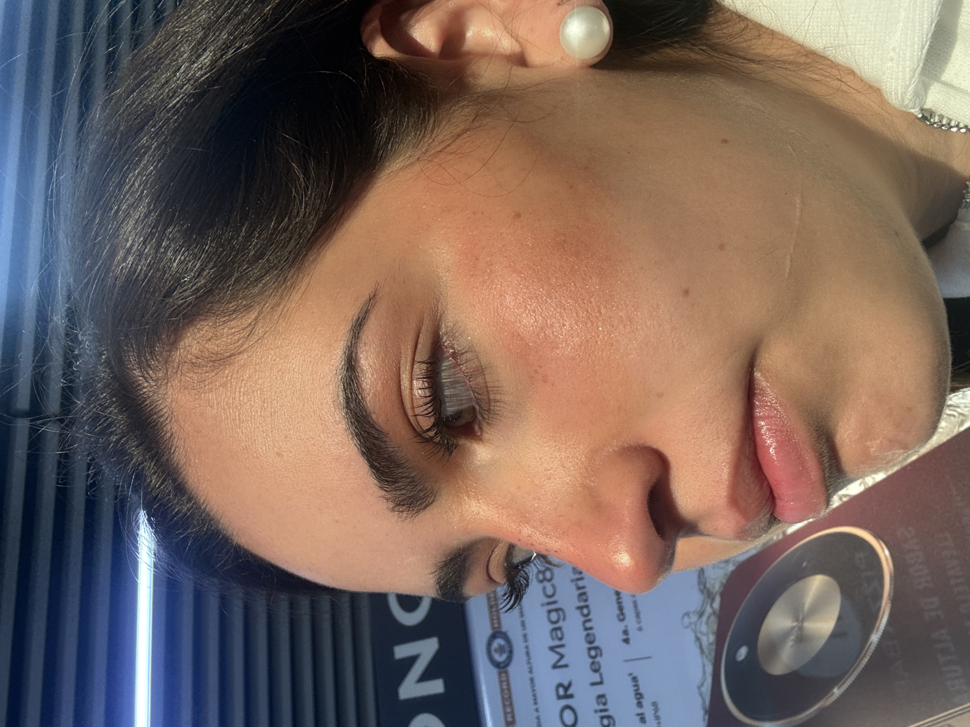 Close-up, a woman with dark hair and a pearl earring is seen in profile. She has dark eyebrows, long eyelashes, and light skin. A portion of a printed document with text is visible near her face. The visible text includes "OR Magic8" and "gia Legendariz." The document is likely marketing material. The location is Mexico City, Mexico.