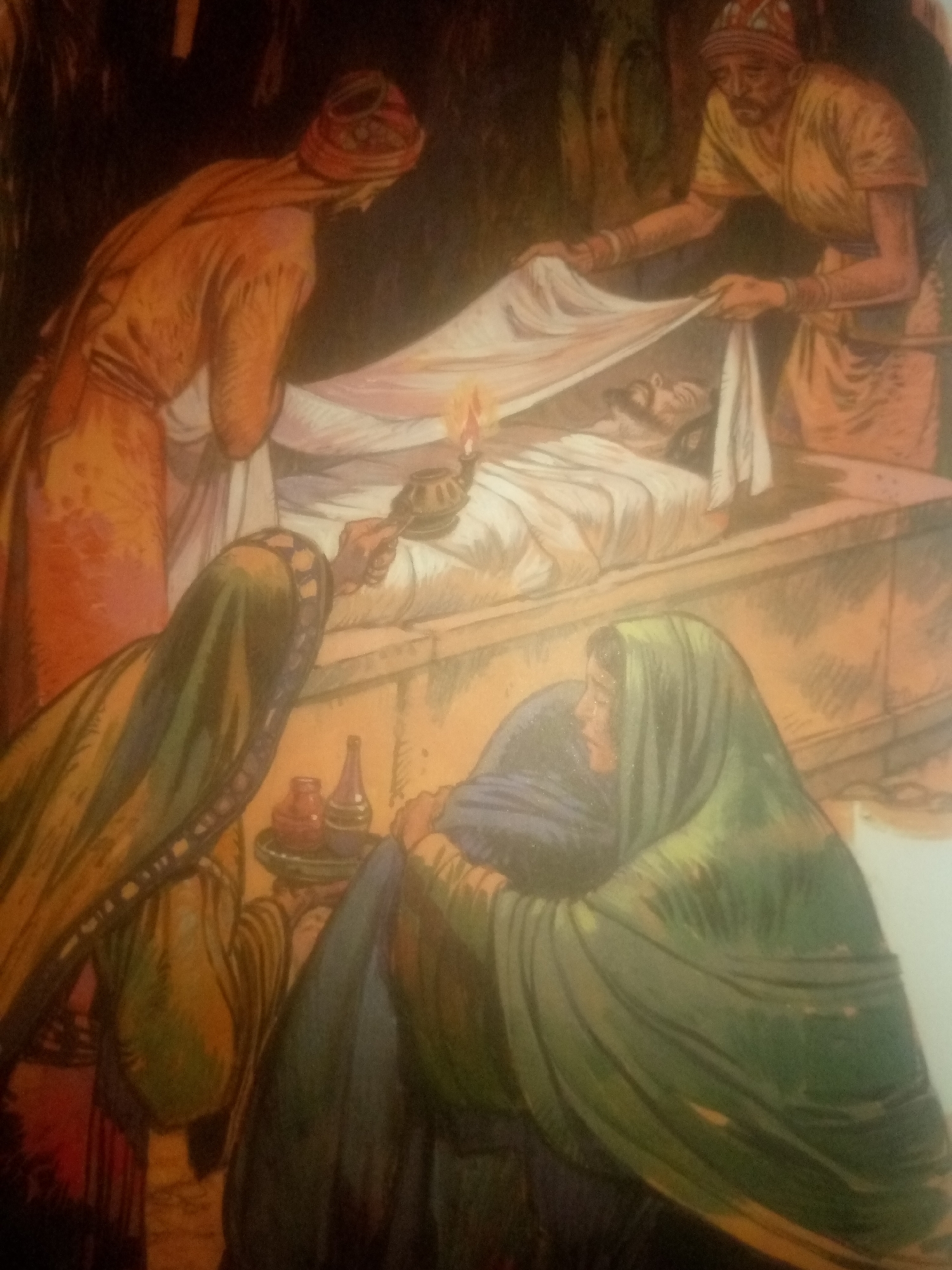 The image depicts a solemn scene with multiple individuals attending to a body lying on a stone slab. A person in an orange robe, their back mostly to the viewer, is positioned to the left, seemingly preparing to cover the body. To the right, another individual in a yellow tunic and a patterned head covering is actively draping a white shroud over the deceased. The deceased, appearing to be a man with dark hair and facial features, is partially visible beneath the shroud.
In the foreground, two figures are kneeling, their faces turned towards the body. One figure wears a green garment and a matching head covering, while the other, to their right, is draped in a dark blue fabric. A small table or ledge in front of them holds several vessels, including what appear to be bottles and jars, possibly for anointing oils or spices. A lit oil lamp is held by a hand, casting a warm glow on the scene, suggesting an act of mourning or preparation for burial.
The background is dimly lit and appears to be an interior space, possibly a tomb or a place of ritual. The overall atmosphere is one of reverence and sorrow. The mention of Jauro Yinu, Nigeria, does not correlate with the visual cues in the painting, which suggests a setting and attire more commonly associated with biblical or ancient Near Eastern contexts rather than contemporary Nigeria.