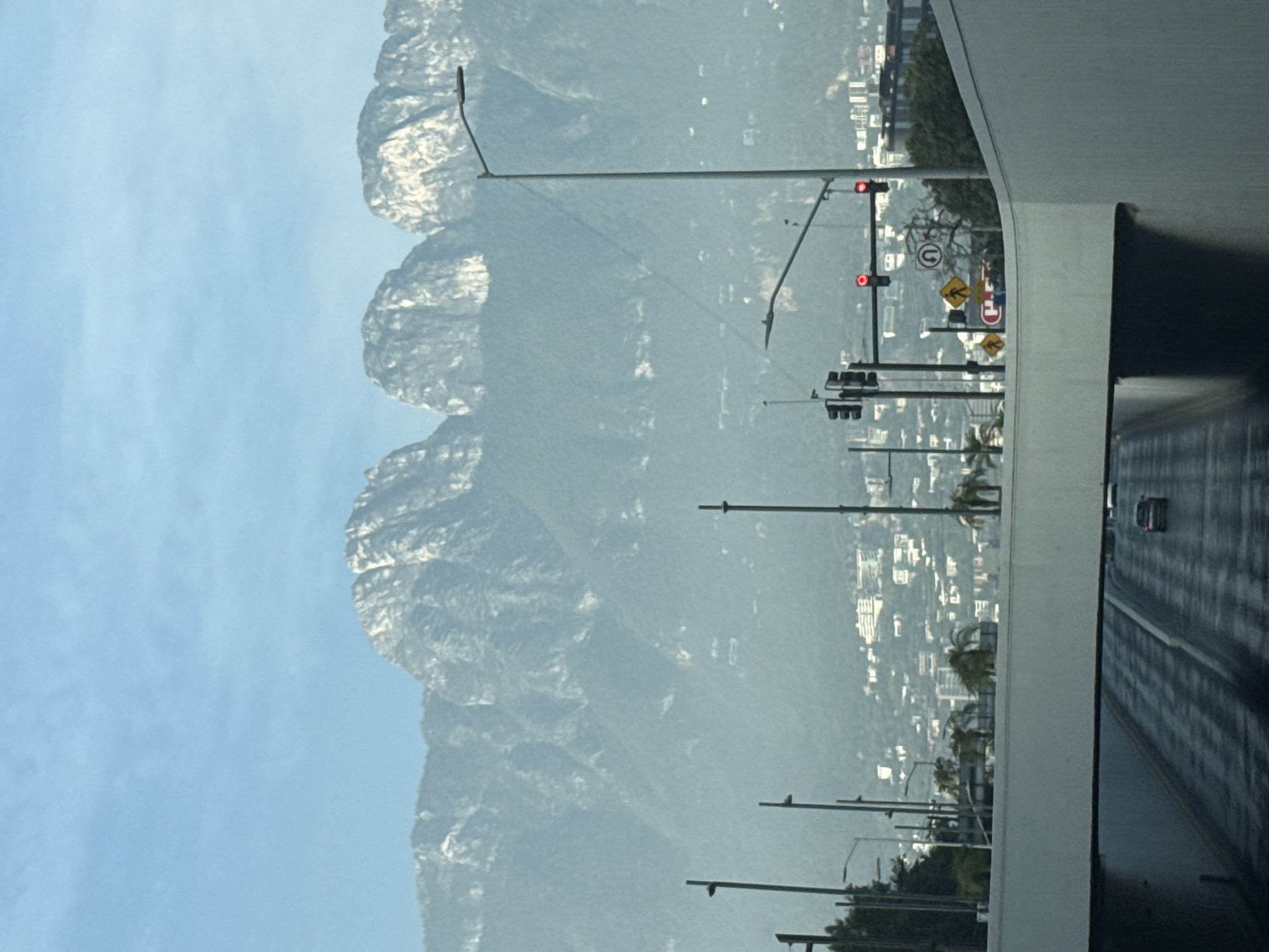 The image depicts a view from inside a tunnel, possibly a highway underpass. Outside the tunnel, a cityscape is visible at the base of a large mountain range, with scattered buildings and vegetation. Streetlights line the road leading towards the mountain. Traffic signals are present, indicating a roadway intersection. A single car is seen driving on the road outside the tunnel. Based on visual cues and the location reference, the scene appears to be in San Pedro Garza García, Mexico.