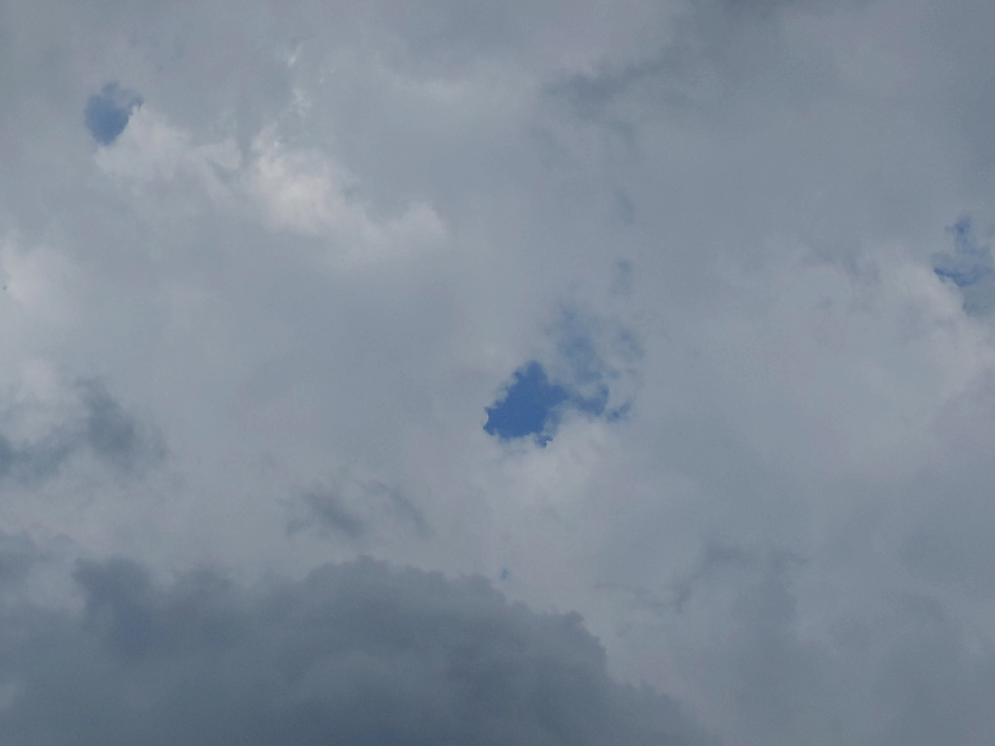 The image shows a cloudy sky with patches of blue visible through gaps in the clouds. The clouds are a mix of light and dark gray, suggesting overcast or partially overcast conditions. There are no discernible landmarks, structures, or natural elements that would allow for the identification of a specific location within Novokuybyshevsk, Russia. The scene is a broad view of the sky.