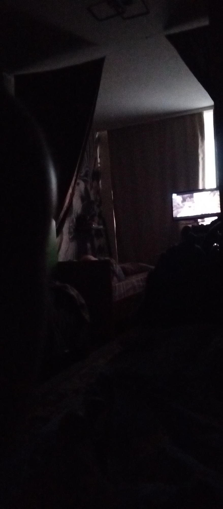 The image depicts a dimly lit bedroom with a television screen glowing in the background. The scene appears to be a personal space, possibly a residence. The focus is on the television and the surrounding darkness, suggesting it's nighttime or the lights are off. The location is identified as Yeruda, Russia.