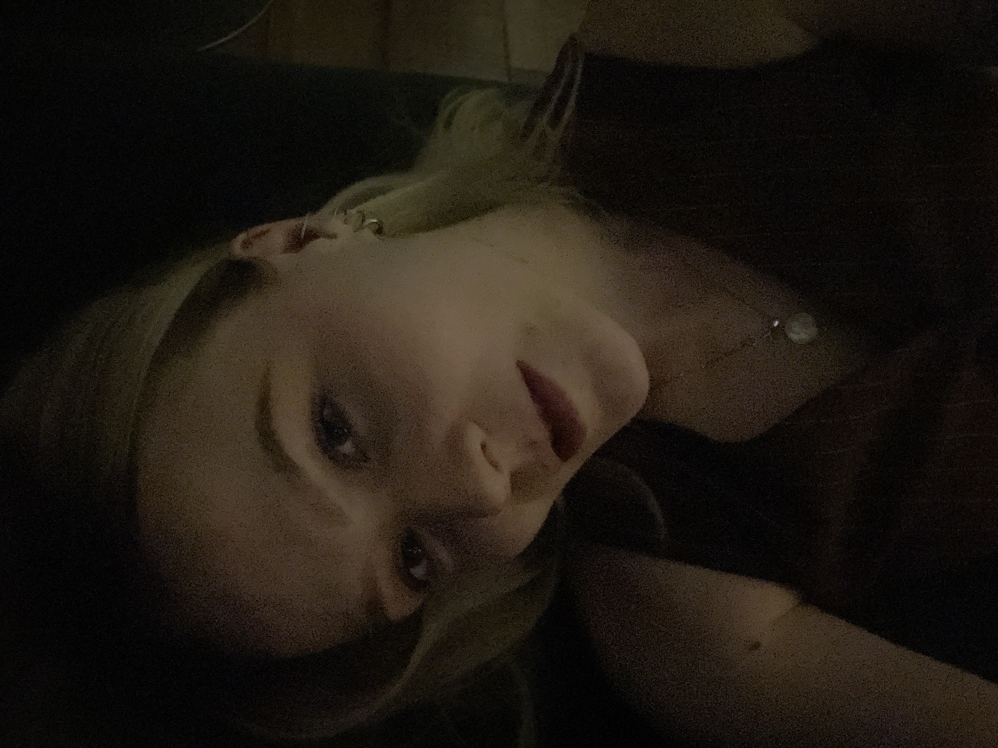 A close-up portrait of a fair-skinned person with light blonde hair. The person's face is angled towards the camera, with eyes open and lips slightly parted. A necklace is visible around their neck. The background is dark and indistinct. There is no evidence of the image being from Khimki, Russia.
