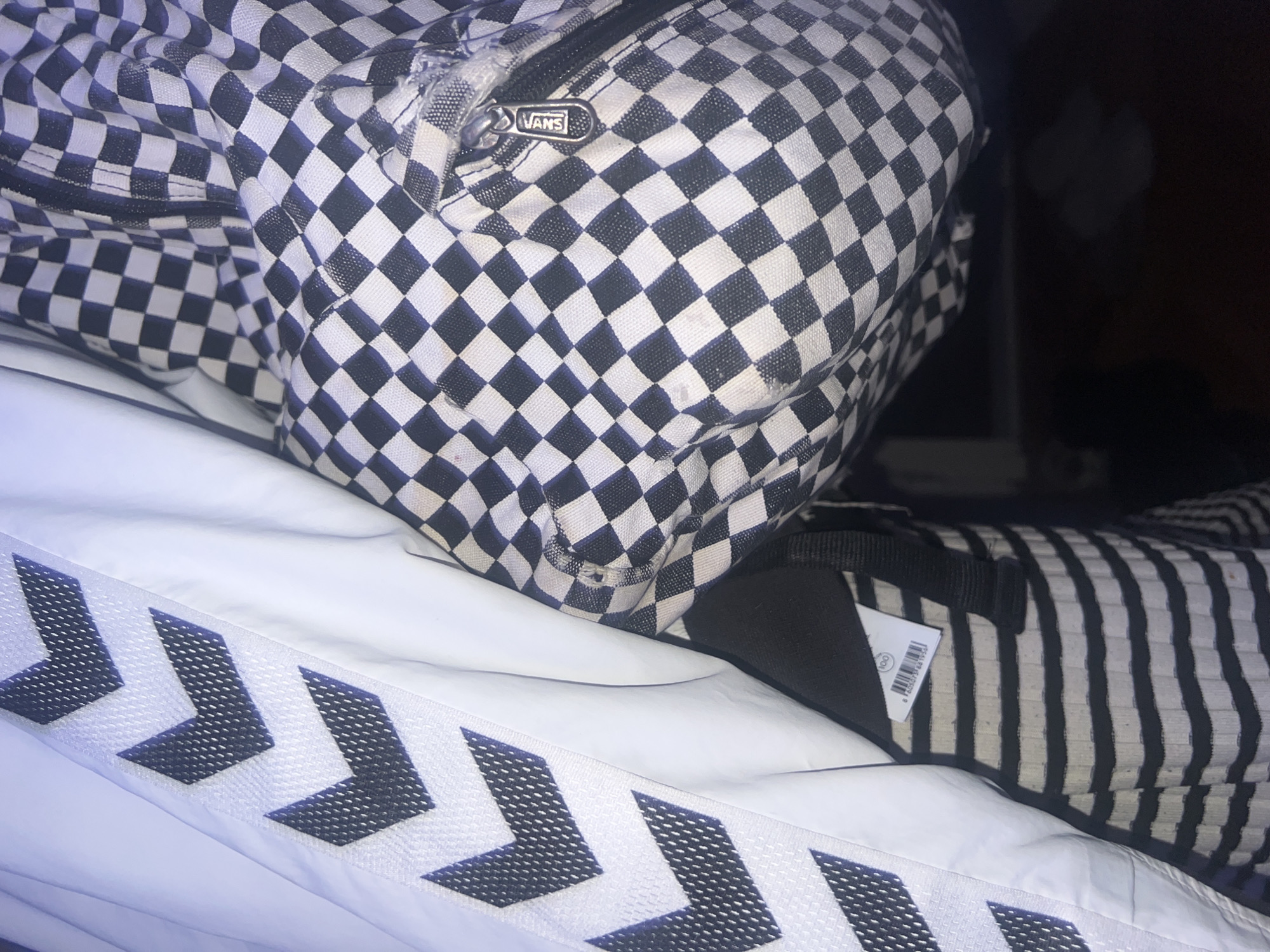 The image shows a partially visible checkered Vans backpack resting on a white surface with gray chevron patterns. Next to the backpack is an item with black and white stripes and a price tag attached. The location in the city of Belgrade, Serbia, is not discernible from the image.