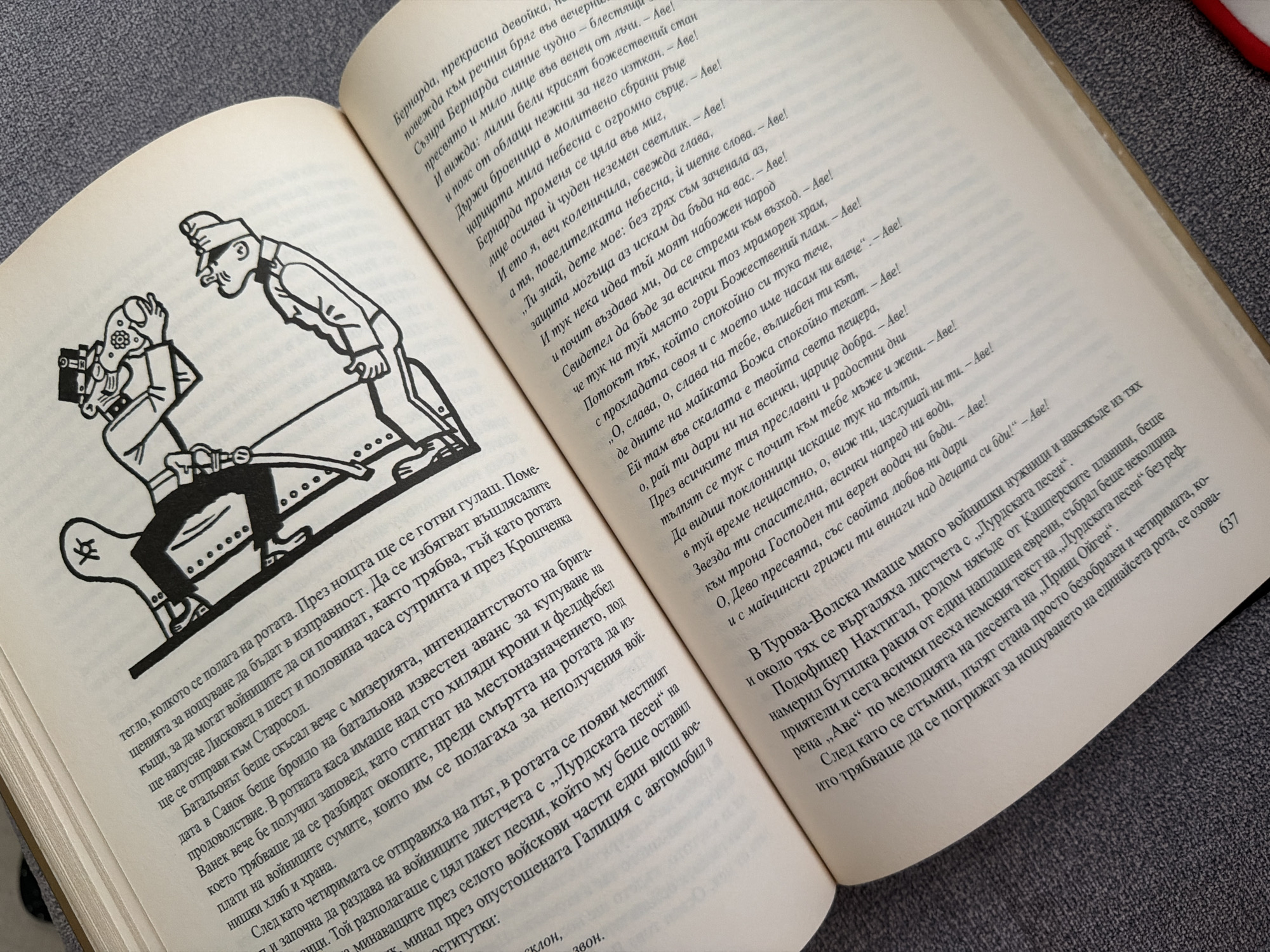 The image shows an open book with a drawing on the left page and text on both pages. The drawing depicts two figures in military-style uniforms. One figure is standing and holding a helmet with a visor and a piece of equipment that resembles a gas mask, while the other figure is kneeling or bending down, looking up at the first figure. The overall style of the drawing is cartoonish and satirical.
The text on the right page is in Bulgarian and appears to be prose, possibly from a novel or story. The text on the left page is also in Bulgarian and contains what seems to be song lyrics or a poem, indicated by the repeated phrase "Аве" at the end of many lines.
The book is lying on a textured gray surface, which could be a table or a carpet. The lighting suggests an indoor environment.
There is no visible indication of the city of Pazardzhik, Bulgaria, or any specific location within it in the image.