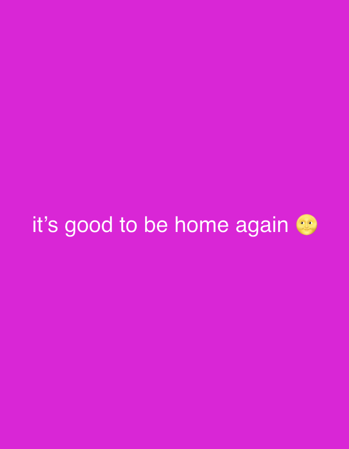 The image is a static, digitally created graphic with a solid magenta background. White text is centered horizontally and towards the bottom of the frame, reading "it's good to be home again" followed by a yellow crescent moon emoji with a face. There are no people, objects, or discernible environmental features within the image. The scene does not contain any elements that would allow for identification of a location in Abuja, Nigeria.