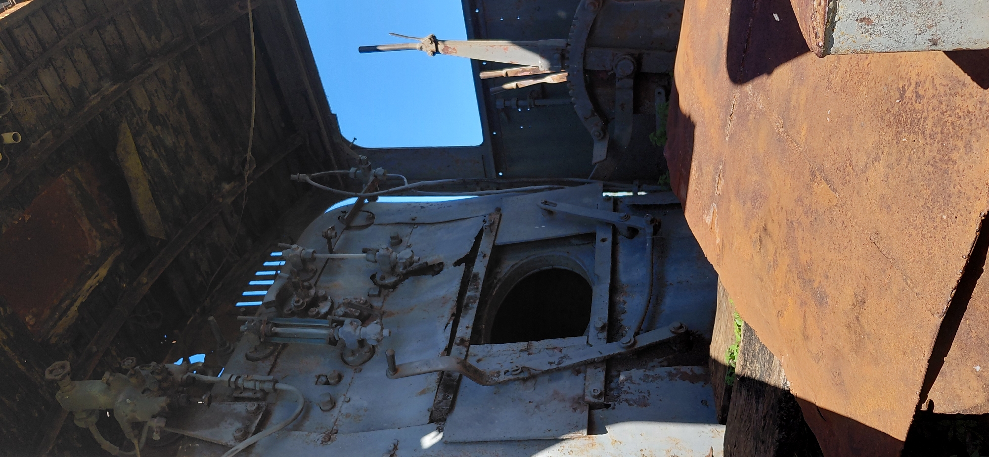 The image depicts the interior of a disused steam locomotive engine. The focus is on the control panel and various metallic components, heavily weathered and rusted. The blue sky is visible through an opening in the rear of the engine. This locomotive is likely part of the collection at the "Museo Ferroviario de Encarnación" (Encarnación Railway Museum) located in the city of Encarnación, Paraguay, where several historic trains are preserved. No people are visible in the image.