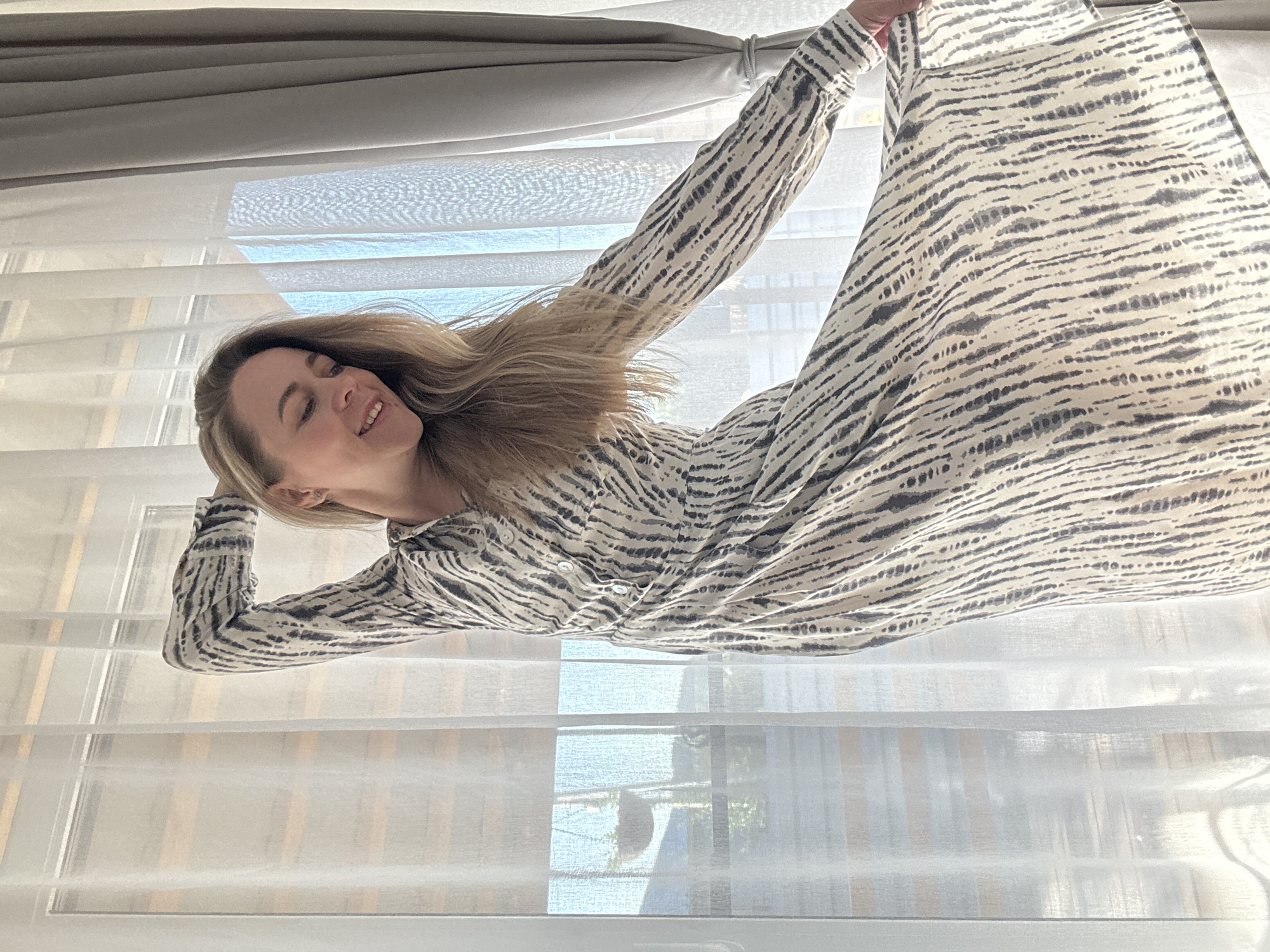 A woman is lying down in front of a window. She is wearing a long-sleeved, zebra-striped dress. The window has white curtains. The location is not discernible as Chaikovsky, Russia from the image.