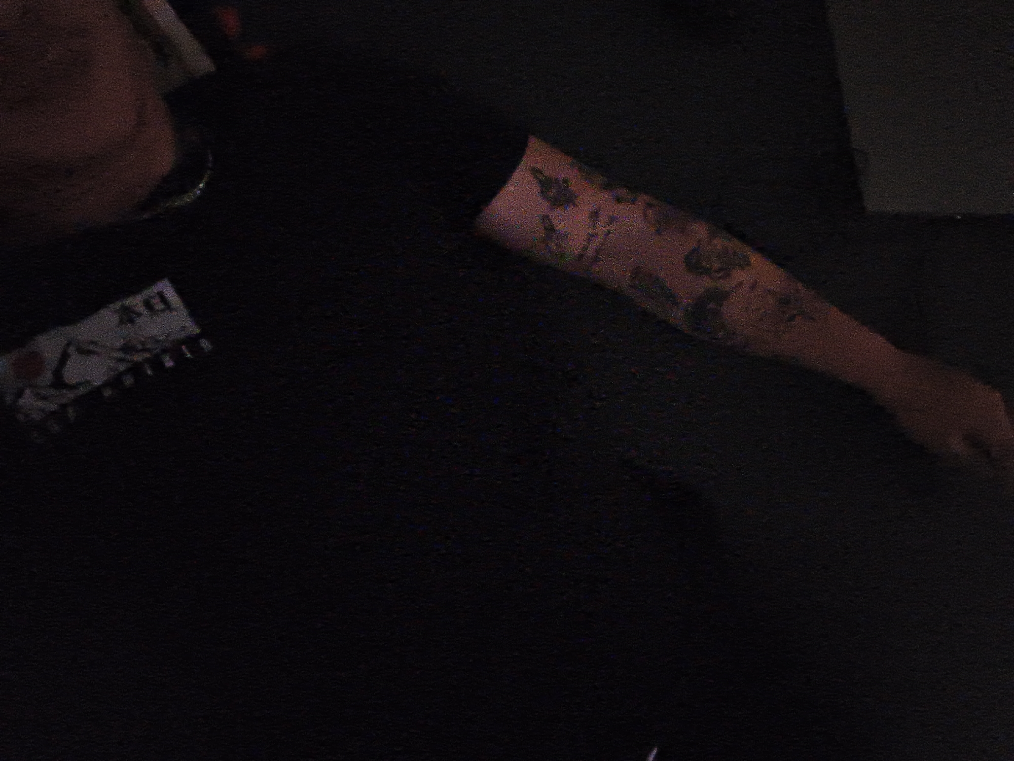 A person's forearm with tattoos rests on a dark surface next to a package with Japanese text. The location is not discernible from the image.