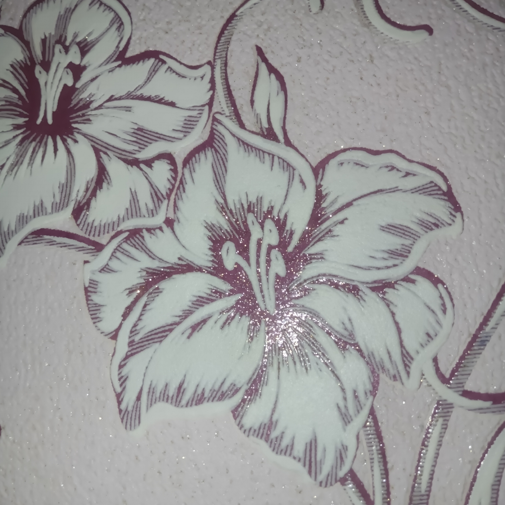 The image depicts a close-up view of a wallpaper pattern featuring large, stylized flowers. The flowers are predominantly white with purple outlines and internal detailing that resembles hatching. Small, glittering particles are scattered across the surface of the image, likely a decorative element of the wallpaper. The background color is a light pink with a slightly textured appearance.
It is impossible to know the exact location in the city of Chaikovsky, Russia, or whether the image was even taken there.