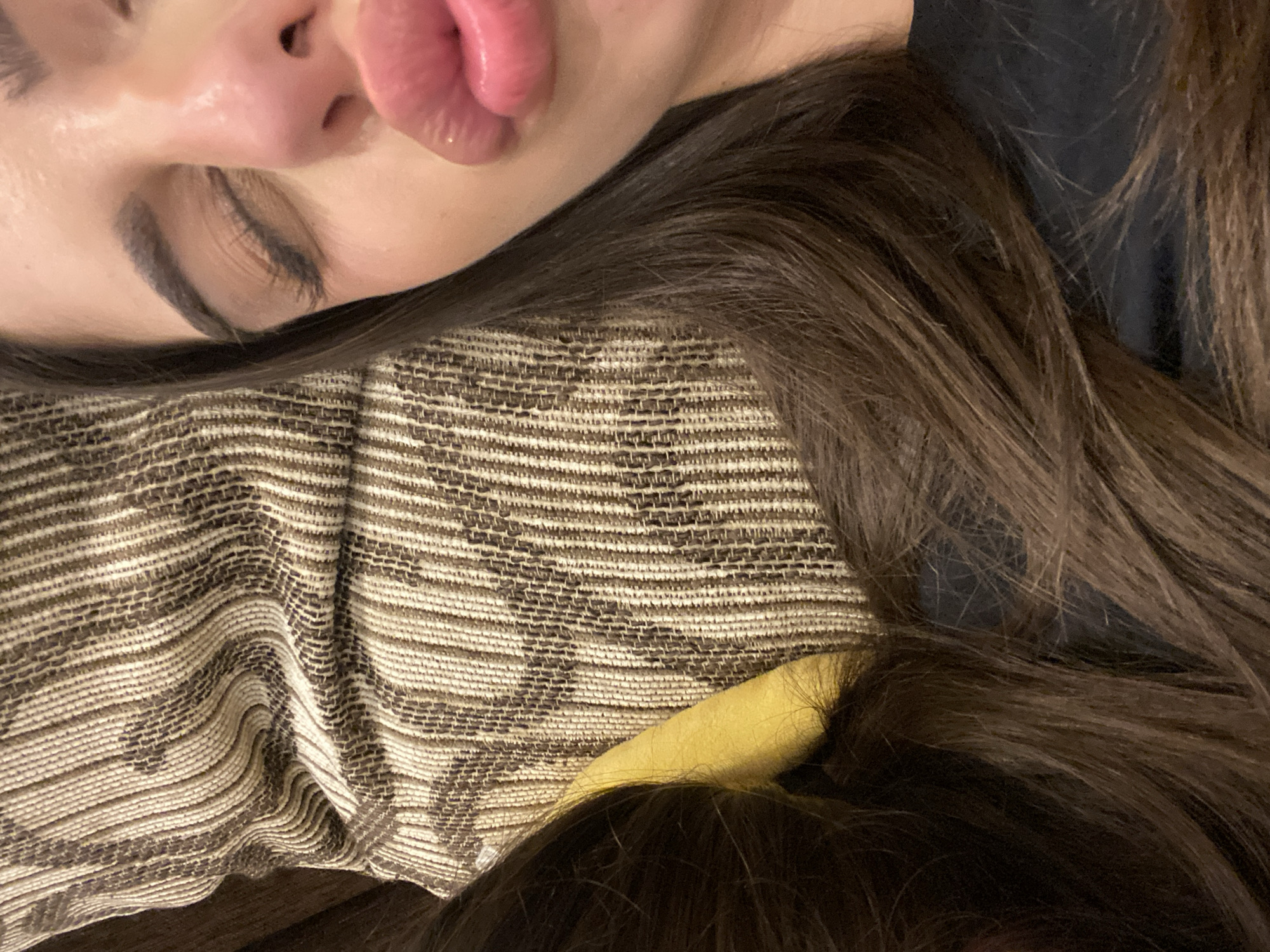 The image shows a person's face and hair resting on a textured surface. The person has closed eyes, a nose, and pink lips. The skin appears smooth. The hair is dark brown and flows around the face and onto the textured surface. The surface is a patterned fabric in shades of brown and beige.
There is no information available to identify the location as Dragovishtitsa, Bulgaria.