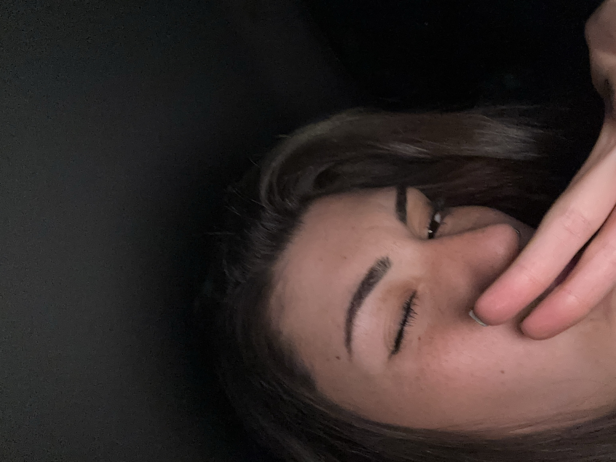 A close-up, dimly lit photograph features a woman's face in the right portion of the frame. Her eyes are closed, and her hand partially covers her mouth and nose. She has fair skin and dark hair. The left portion of the frame is dark and featureless. The photo offers no specific details to indicate the location is Sofia, Bulgaria.