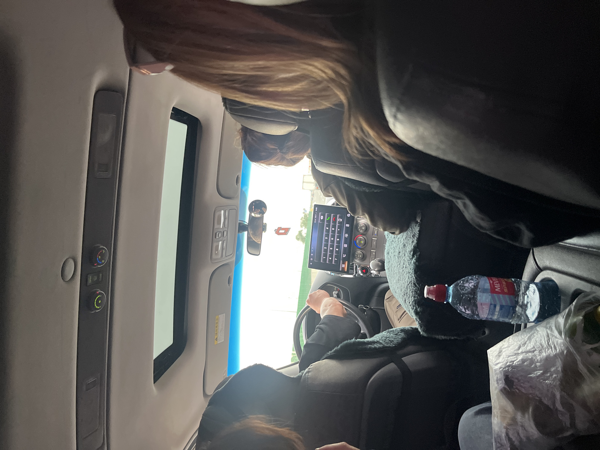 A view from inside a car in Stalskoye, Russia. One person is driving while a passenger occupies the front seat. A touch screen infotainment system is visible in the dashboard. A water bottle is next to the front passenger.