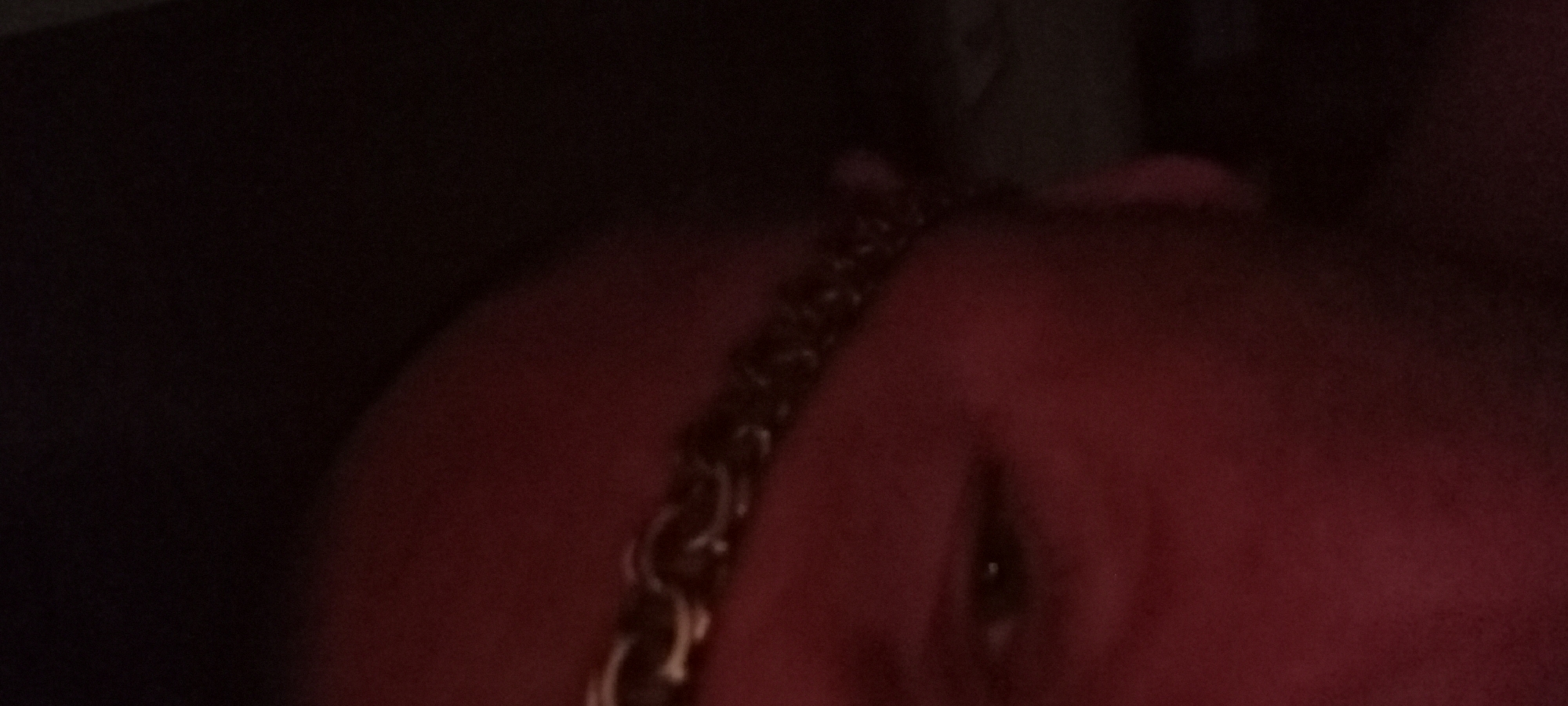 The image is a close-up, dimly lit, and blurry photograph of a person's face. A chain is visible across the forehead and upper part of the face. The lighting is predominantly red, suggesting a low-light environment or possibly a colored light source. The background is dark and indistinct. The image is not located in Kryvyi Rih, Ukraine.