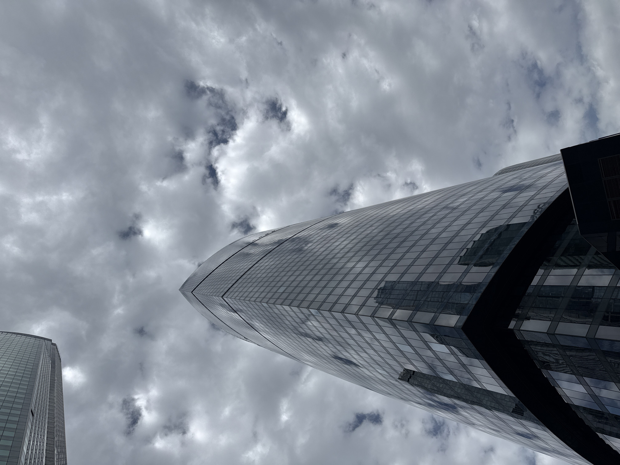 A low-angle shot depicts a modern skyscraper under a cloudy sky. The building features a curved, glass-paneled facade that reflects the surrounding clouds and the structures opposite it. The structure appears to be in a built-up urban environment and is located in Khimki, Russia.