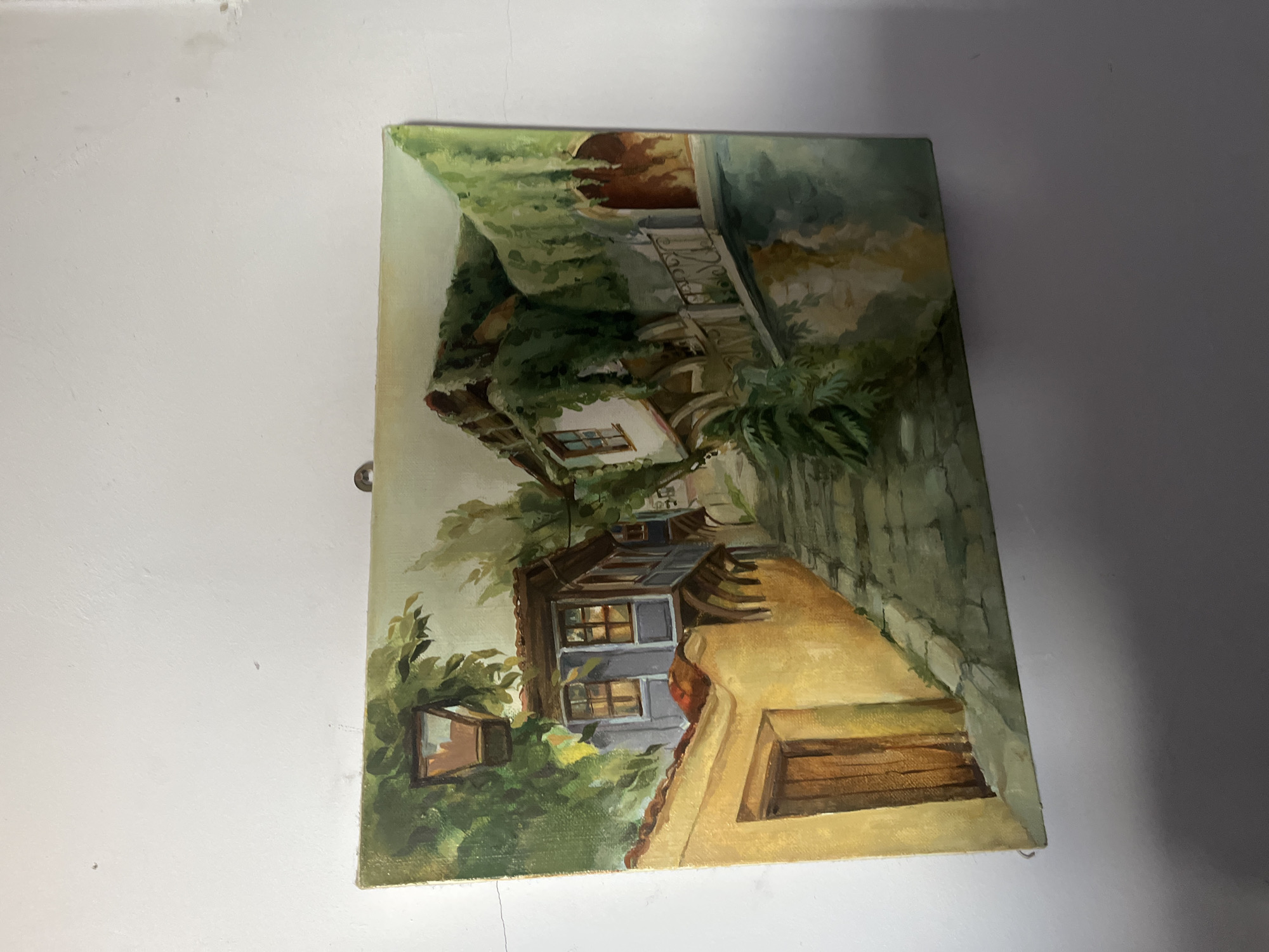 The image shows a painting depicting an old house in the city of Goce Delchev, Bulgaria. The style is impressionistic. The painting includes the house, greenery, and a road in a naturalistic environment.