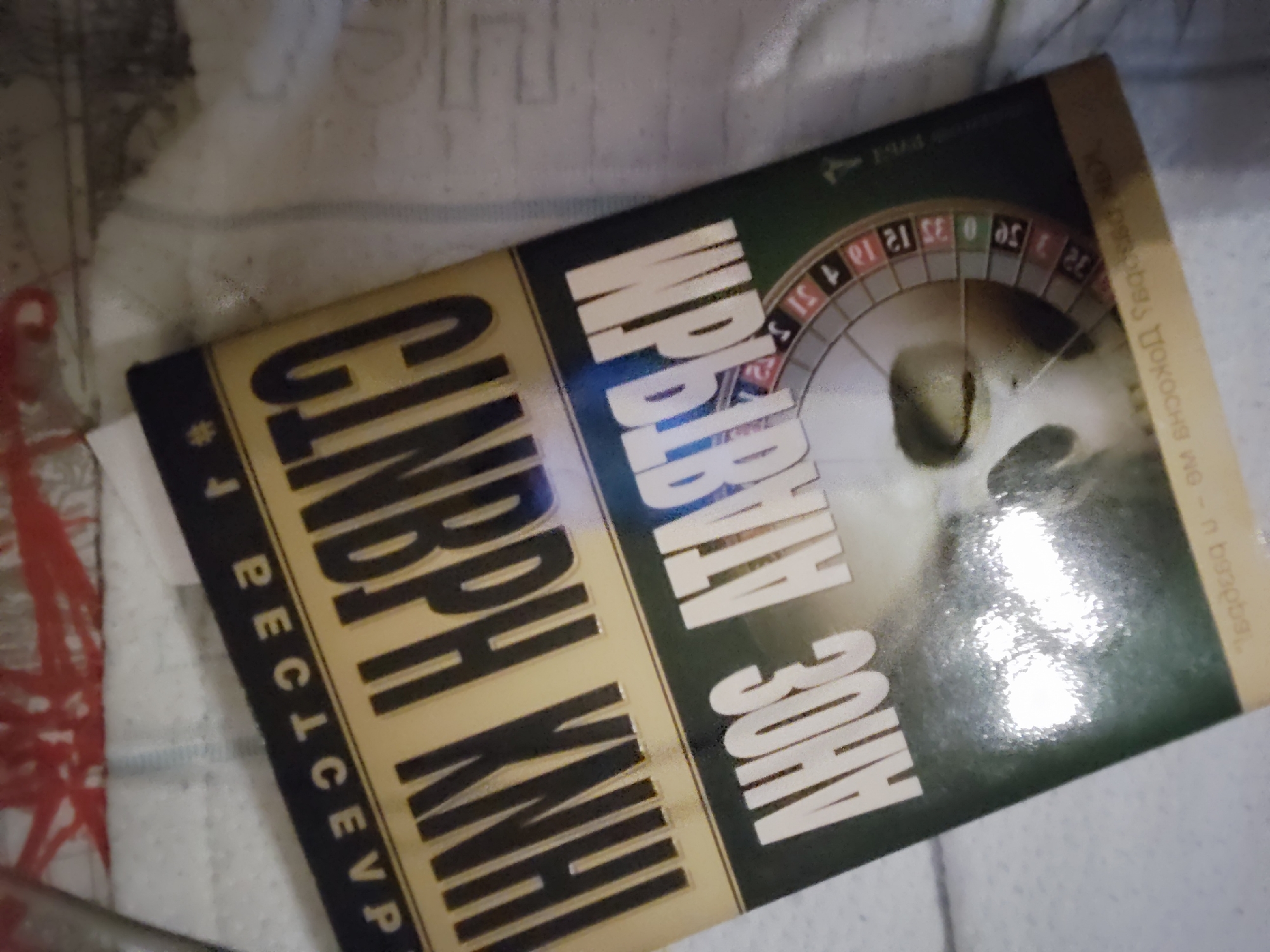 The image shows a book titled "Първият в зона". The book appears to be a detective novel written by Gindrih Kni, as indicated by the text "Гинрих Книг * Ресеп". The cover design includes a roulette wheel and a skull. I can't locate the location of the image in Sofia, Bulgaria with the available data.