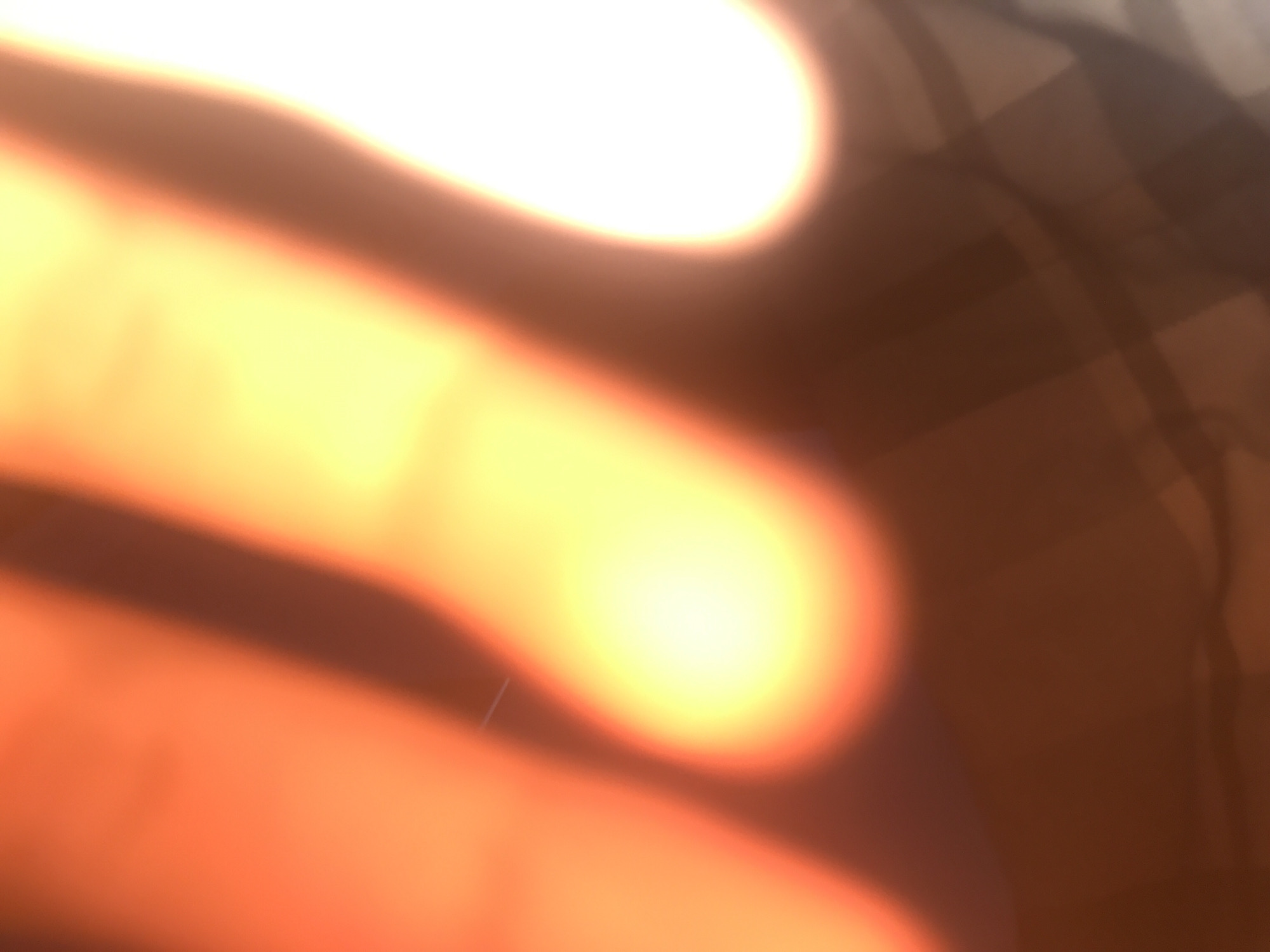 The image is severely blurred and overexposed, making it impossible to determine the specific location or identify any objects, people, or actions. The dominant colors are shades of orange, yellow, and brown. There are some linear patterns visible in the upper right portion of the image, but their nature is unclear. It is not possible to discern if the image was taken in Yerevan, Armenia or anywhere else.