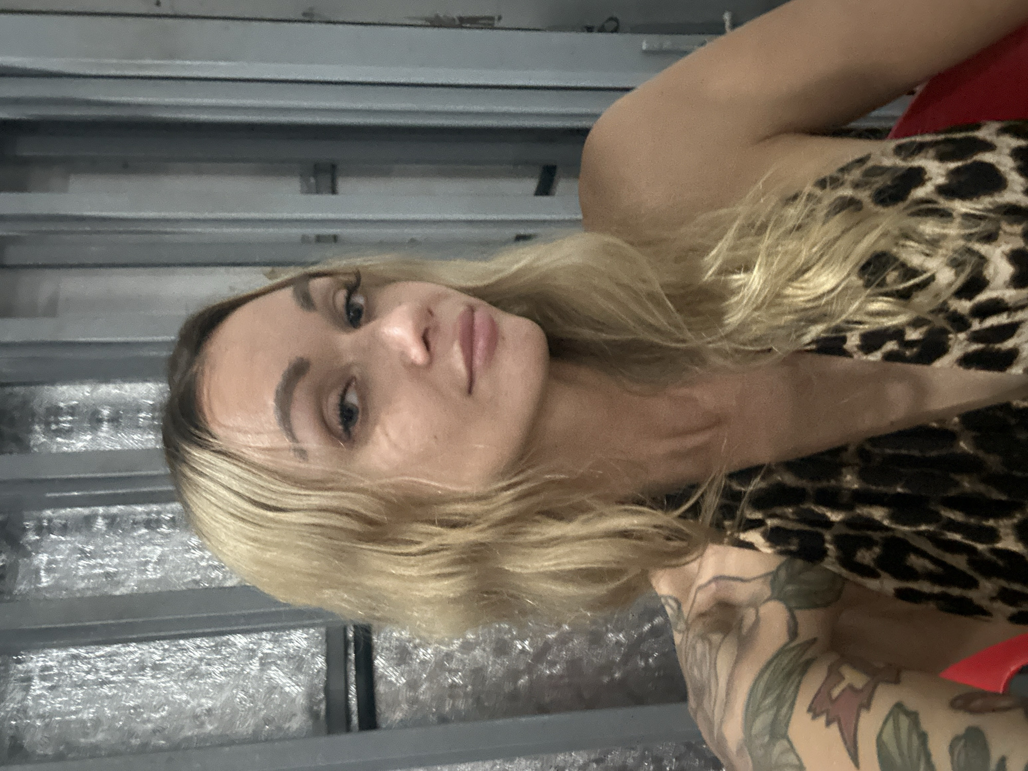 A woman with blonde hair and tattoos on her arm is lying down, wearing a leopard print top. The background appears to be a metallic structure. The location of Phu Thuy Ward, Vietnam is not supported by the image.