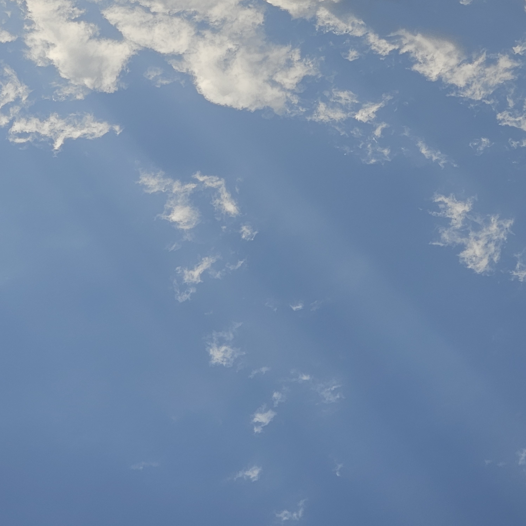 The image is a close-up, full-frame shot of a bright blue sky dotted with scattered white cumulus clouds. There are faint, diagonal light rays visible, suggesting the sun is shining from the upper left. The clouds are wispy and varied in size, some appearing as small tufts, others more substantial. The overall scene depicts a clear day. The image was taken in Andijan City, Uzbekistan.