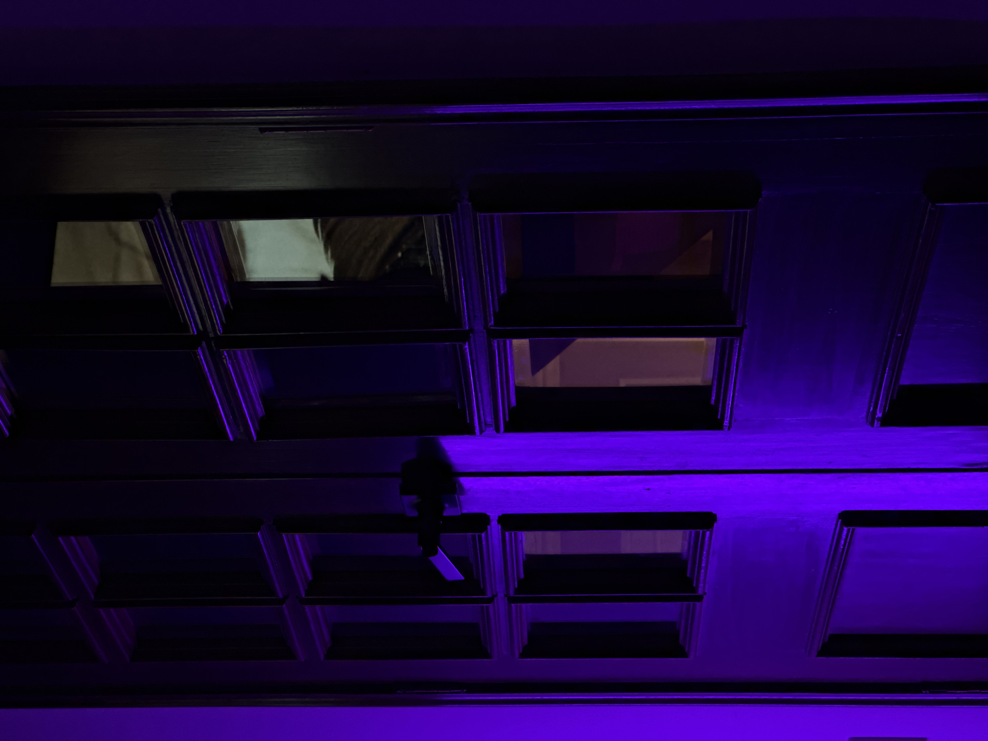 Low-angle shot of a coffered ceiling, illuminated by purple light. In the center, a small human figure is suspended from a ceiling beam. The location is presumed to be in Mexico City, Mexico.