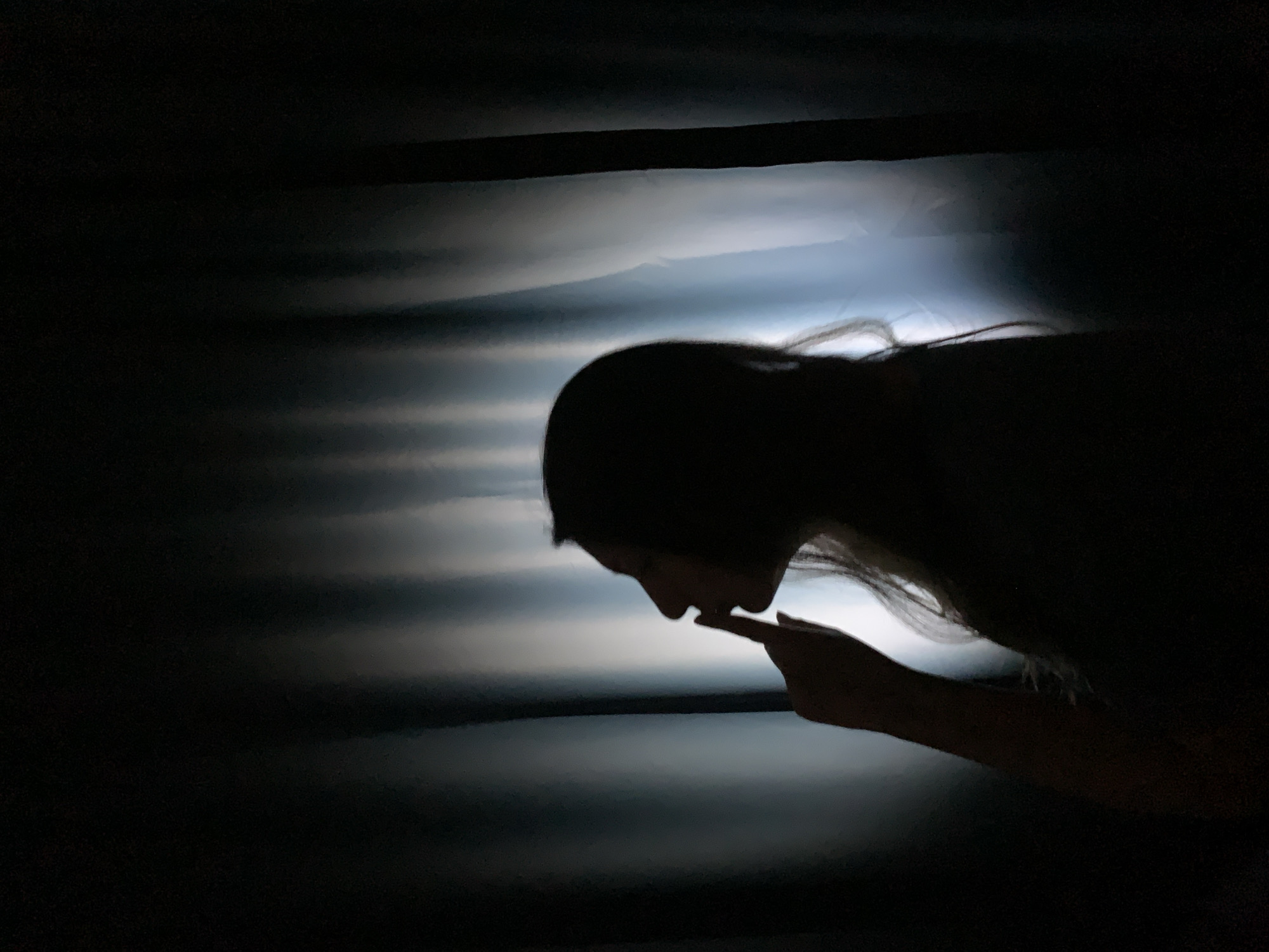 The image depicts a dimly lit scene with a person's silhouette against a lighter background. The person is leaning forward, with their finger near their lips. The overall environment is dark, with the light source behind the person, creating a stark contrast. The exact location in Chaikovsky, Russia cannot be determined from this image.
