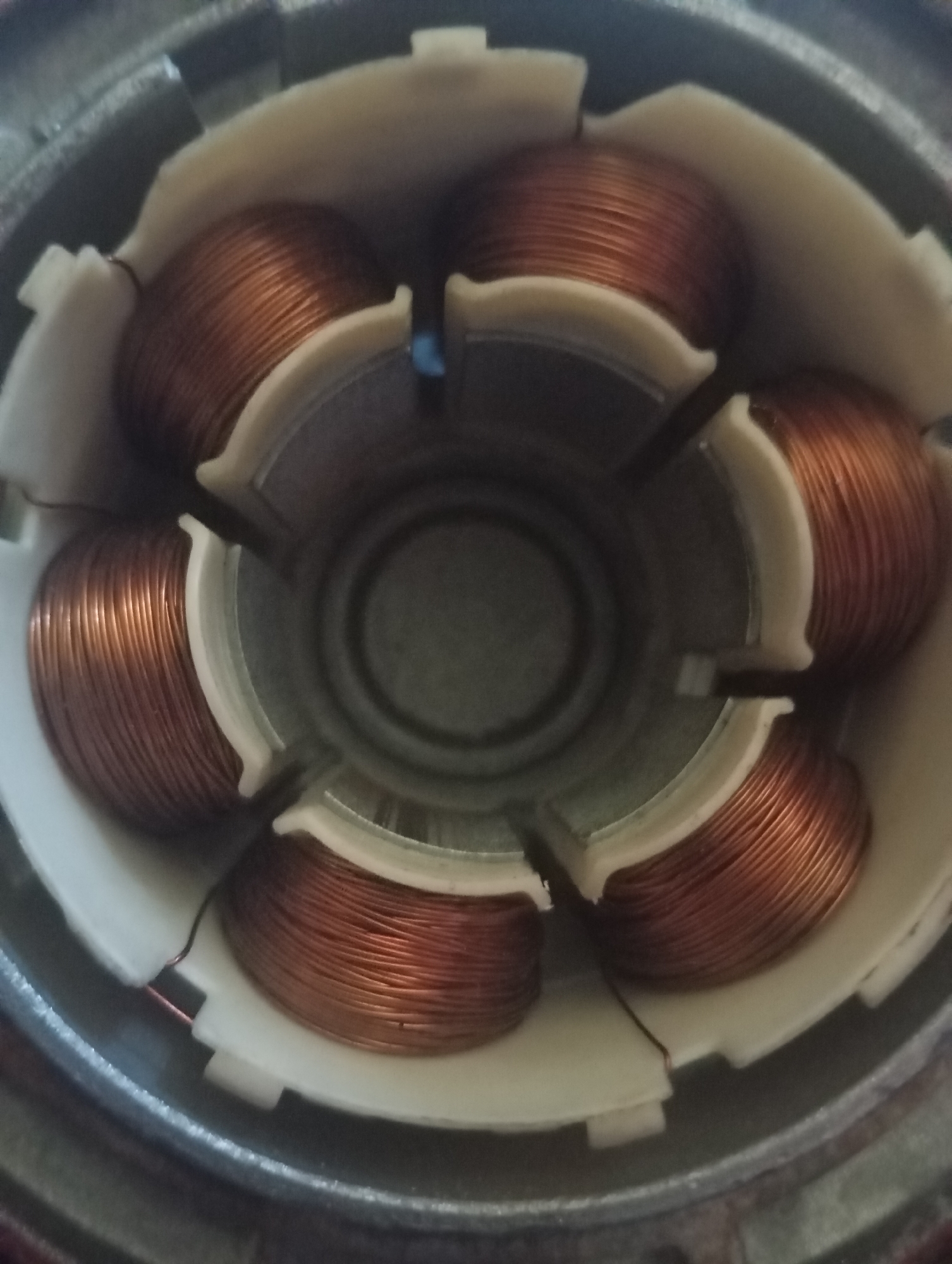 The image shows the interior of an electric motor stator, featuring six copper wire windings arranged in a circular pattern. These windings are encased in a white plastic housing. The overall setting appears to be indoors, likely a workshop or repair area. The image does not contain any information about its location in Sofiivska Borshchahivka, Ukraine, nor does it depict any people, actions, or interactions. The focus is exclusively on the mechanical components of the motor.