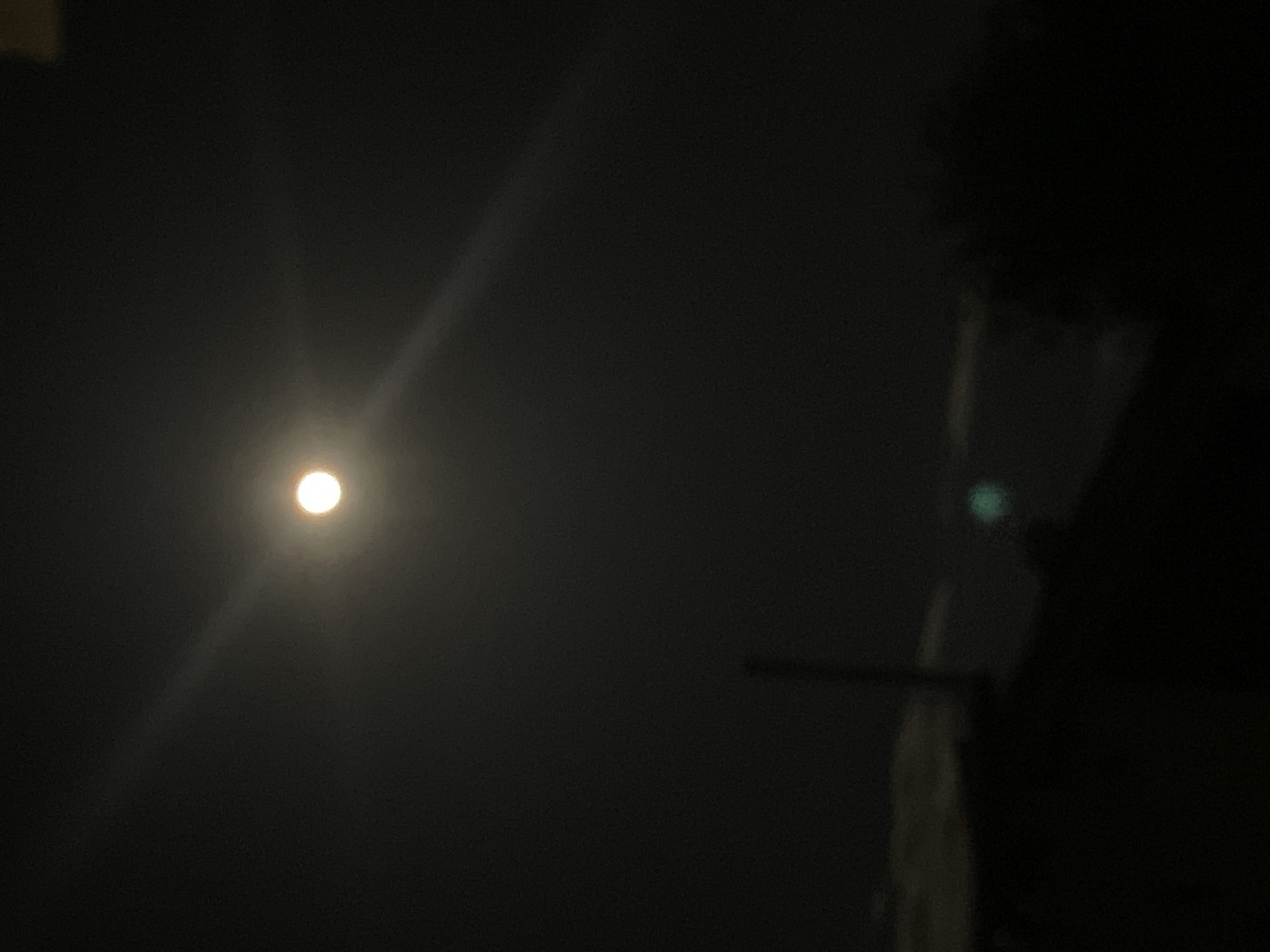 The image depicts a night scene with a bright, circular light source in the upper left portion of the frame. This light source, likely the moon, emits rays of light. The overall scene is dark, with the majority of the image consisting of a black or very dark gray area. In the right part of the image, some undefined objects (maybe parts of a building or a structure) are present but are mostly obscured by darkness. A horizontal bar is also visible in the lower-right area. Given the limited information and the darkness of the image, specific details about the location in Sofia, Bulgaria, cannot be determined.