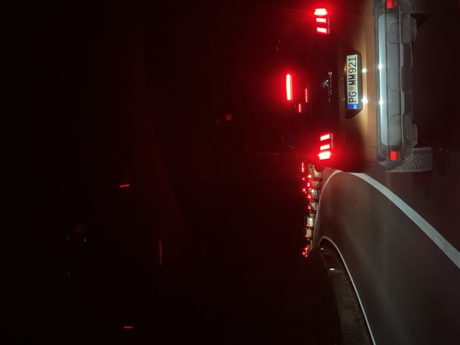 A nighttime traffic jam with rows of red tail lights illuminating the darkness. The closest vehicle, a tan-colored SUV, displays a license plate "PG MM921". A partial view of the highway lane markings are visible. The road seems congested.