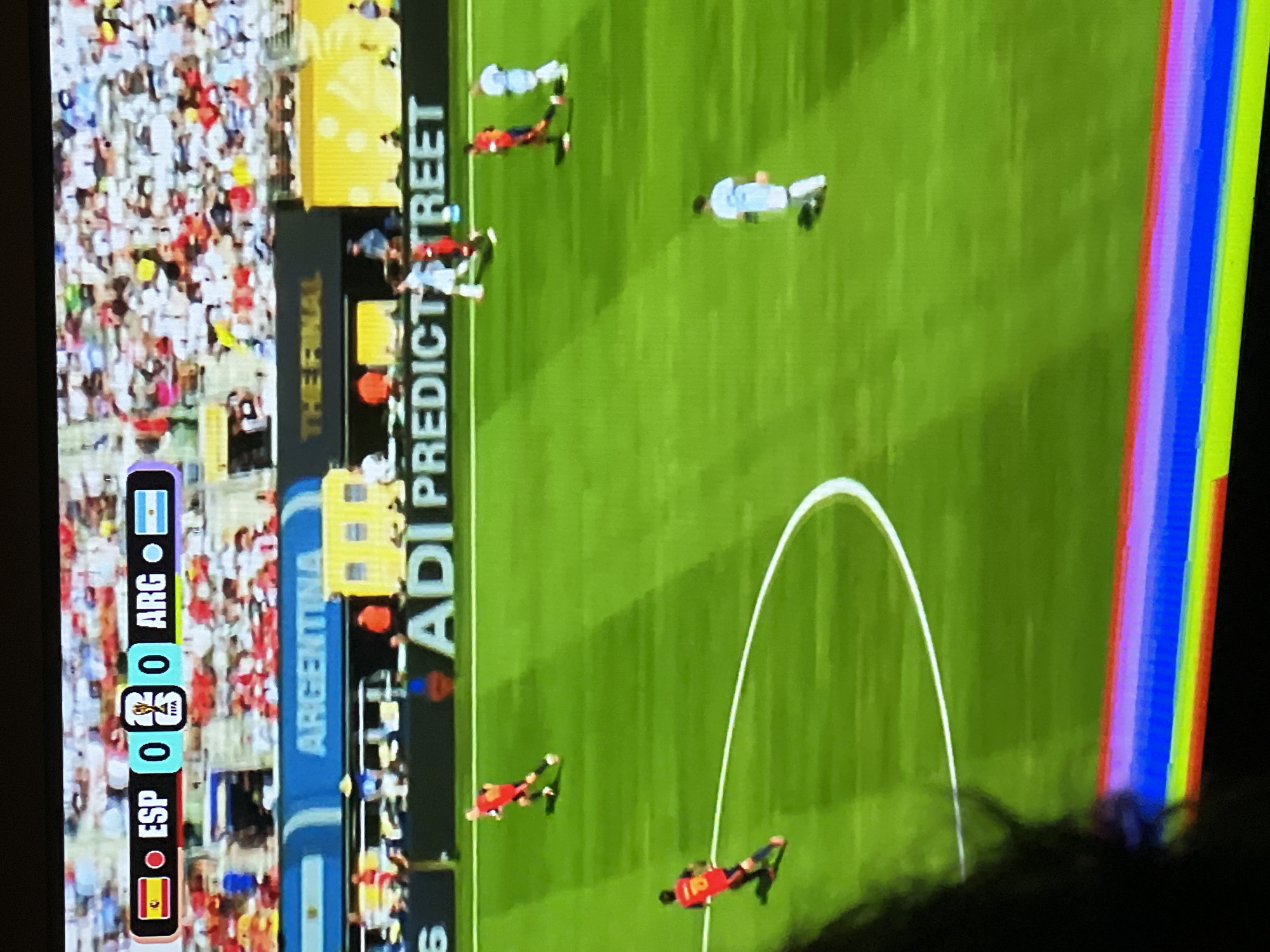 The image shows a soccer match on a large screen. The scoreboard displays "ESP 0 - 0 ARG". There are players on the field in red and light blue uniforms. Spectators are visible in the background. Banners in the background read "ARGENTINA" and "THE FINAL". A digital advertisement with the text "ADI PREDICT STREET" is also visible. The scene appears to be an indoor or covered venue, possibly a stadium or arena, given the screen and the lighting. The image is a photograph of a screen, with some distortion and color bleed at the bottom edge. The location in Moscow, Russia, is not indicated in the image.