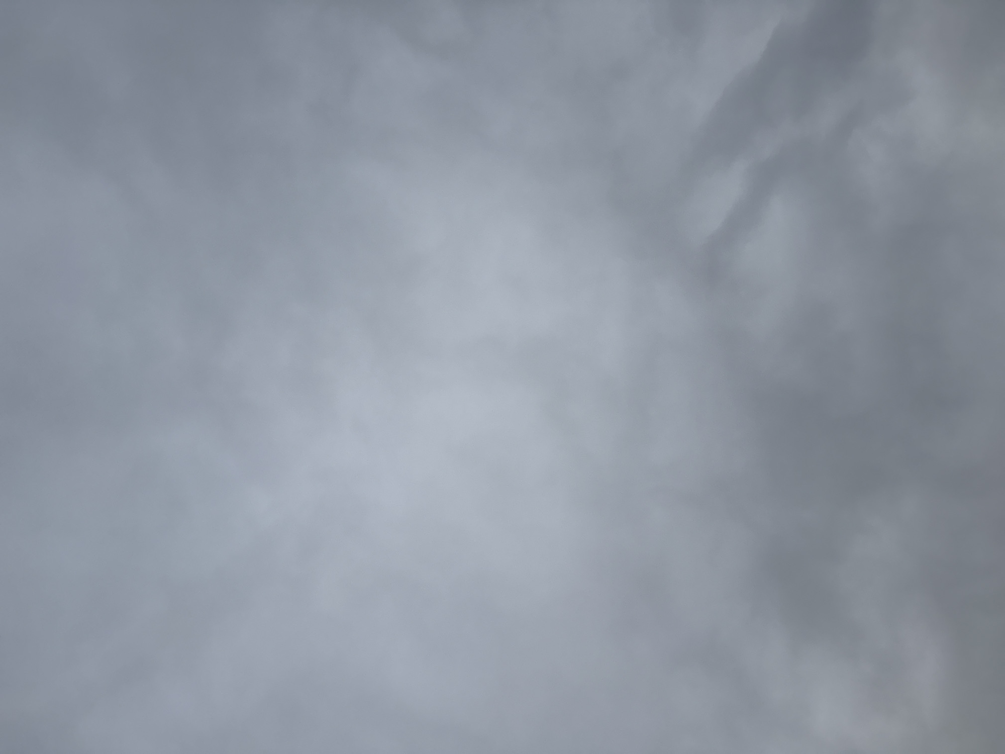 A cloudy sky over Bad Sachsa, Germany, displays a uniform grey overcast. The clouds are dense and appear to be a stratiform layer, obscuring any direct sunlight. The texture of the clouds is soft and diffused, with subtle variations in shade suggesting depth and movement. No distinct cloud formations or celestial bodies are visible. The overall impression is one of a subdued, muted atmosphere typical of overcast weather conditions. The image is taken from a low angle, looking upwards.