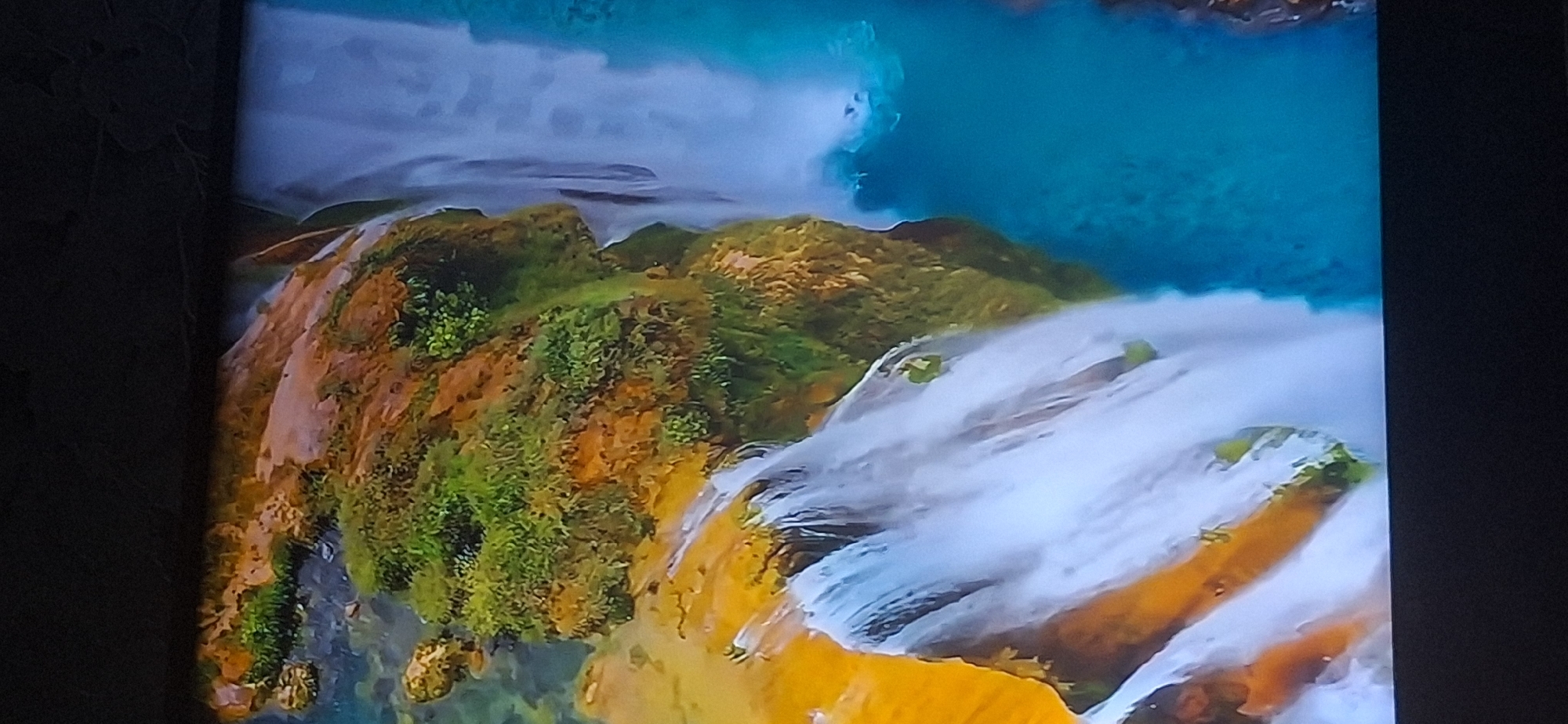 The image displays a close-up, vertical view of a multi-tiered waterfall cascading down rocky, vegetation-covered cliffs into a vibrant turquoise pool of water. The terrain is characterized by ochre-colored rock formations interspersed with lush green moss and foliage, indicating a humid and well-watered environment. Water flows in white sheets and streams over ledges, creating a dynamic and picturesque natural scene. The image does not depict any urban elements or any recognizable landmarks within the city of Bila Tserkva, Ukraine. The scene is solely focused on the natural beauty of the waterfall and its surroundings.