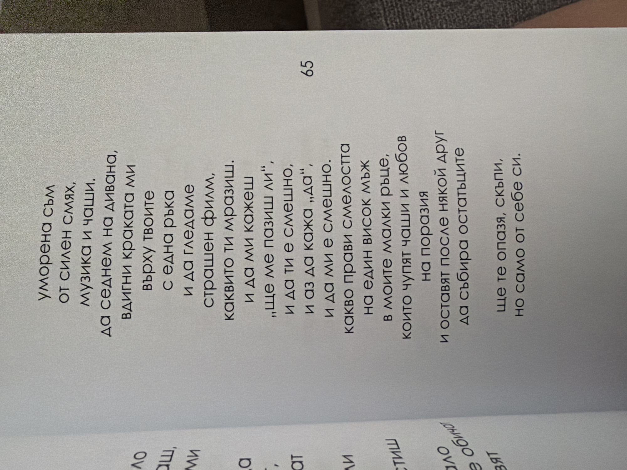 The image shows a close-up of an open book with Bulgarian text. The text is printed in a dark font on a light-colored page. Some of the text is slightly out of focus due to the angle of the photograph. The page number "65" is visible on the right side of the page. The left side of the image shows the edge of another page with some partially visible Bulgarian text. The book appears to be lying flat on a surface, with the spine visible on the left. The lighting suggests an indoor environment. There are no visible people or any specific geographical markers that would indicate the city of Pazardzhik, Bulgaria.
