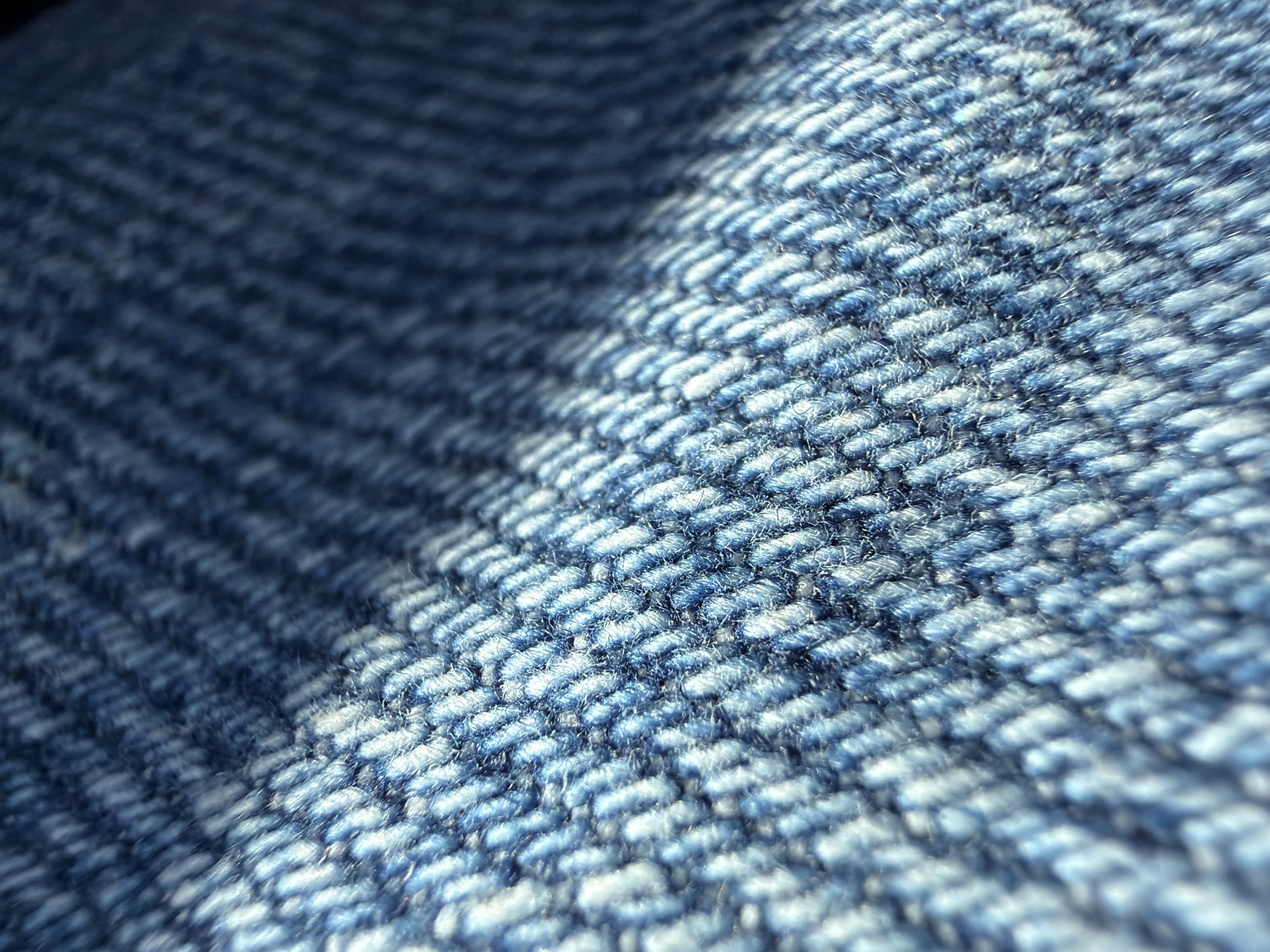 The image shows a close-up of blue denim fabric. The weave pattern is visible, with alternating blue and white threads. Part of the fabric is shadowed. The location is unknown; the image provides no data to establish it is in Varna, Bulgaria or any specific location.